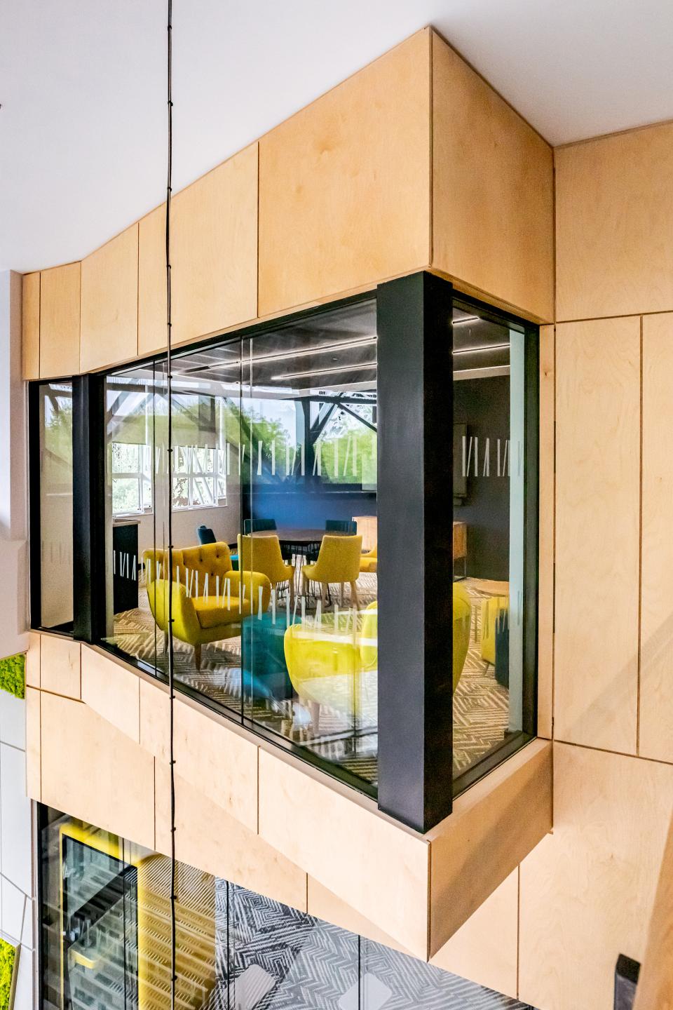 Modern glass-walled meeting room featuring vibrant yellow and blue seating in a flexible workspace environment.