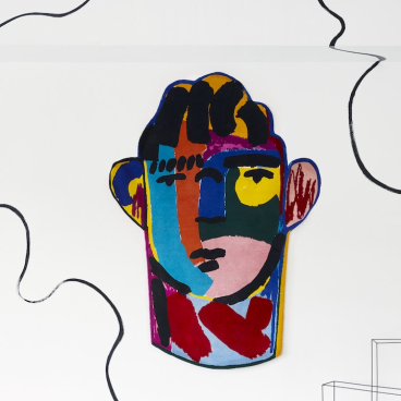 Colorful wall art by John Booth featuring a stylized face, complemented by geometric elements in a modern interior setting.