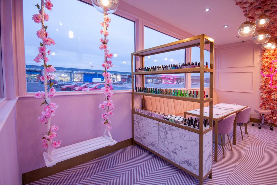 Pastel pink interior of Nailbox featuring a shelf of nail polish, floral accents, and a seating area.