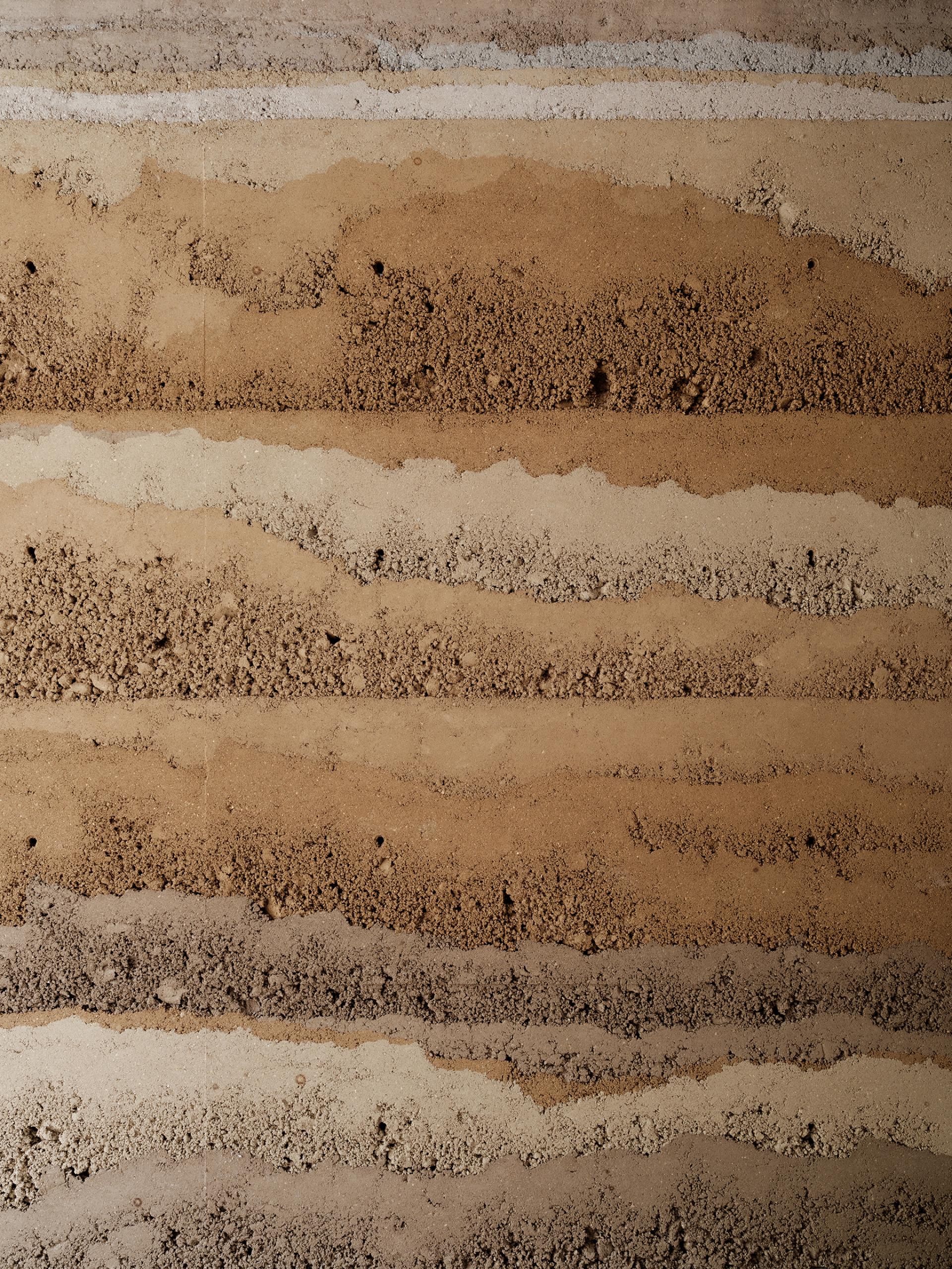 Natural rammed earth wall finish showcasing textured layers in earthy tones, highlighting Clayworks' sustainable design approach.