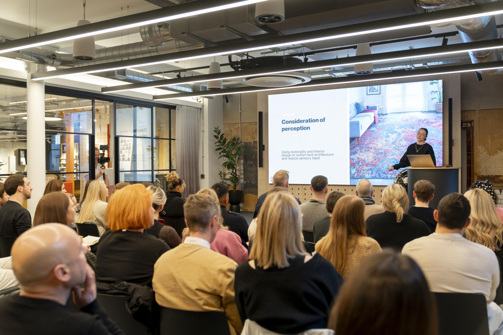 Audience engaged in a presentation on inclusive design strategies addressing neurodiversity and sensory perception in architecture.