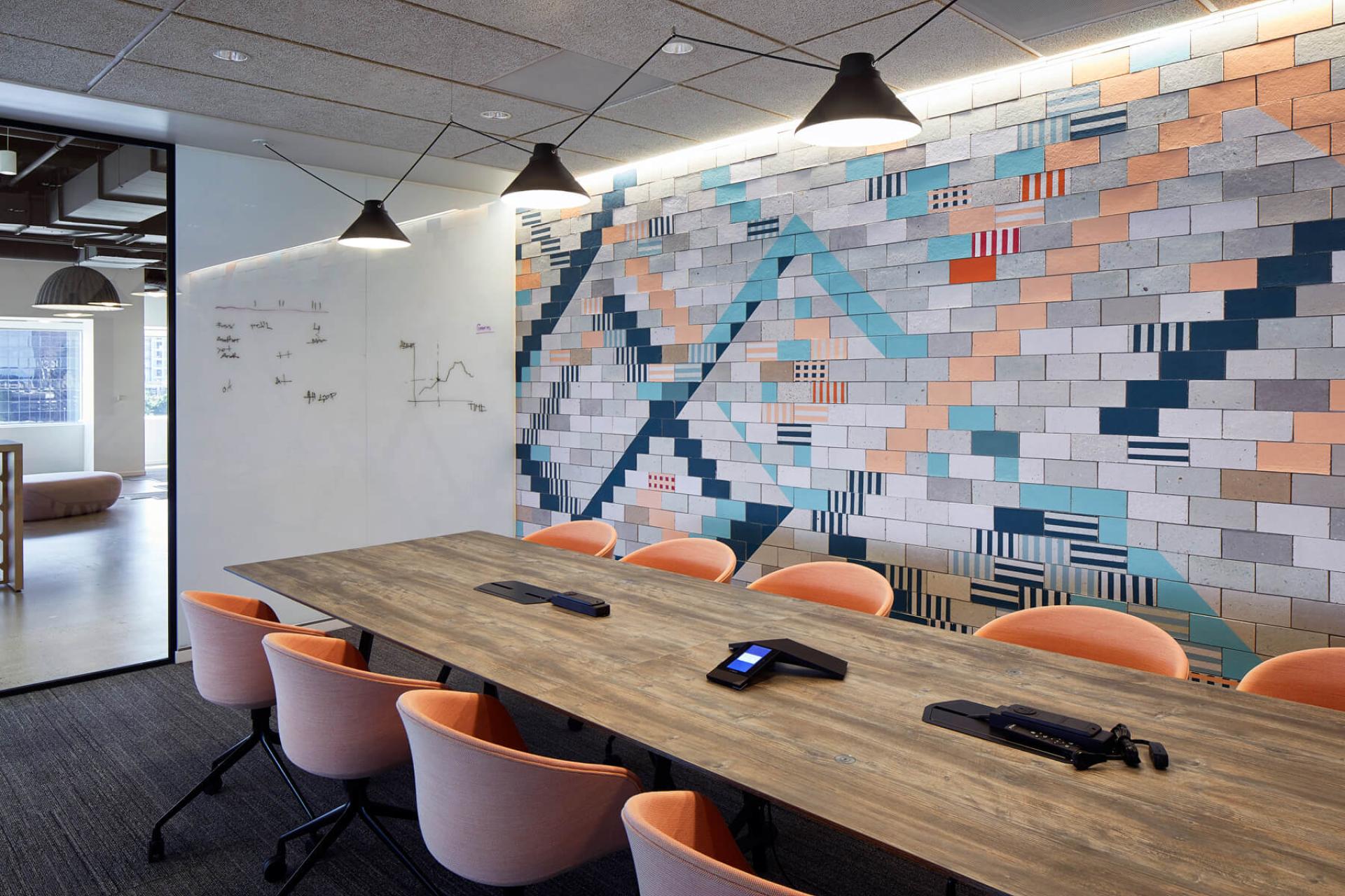 Modern conference room with a colorful mural, wooden table, and orange chairs, showcasing Dear Human's design aesthetic.