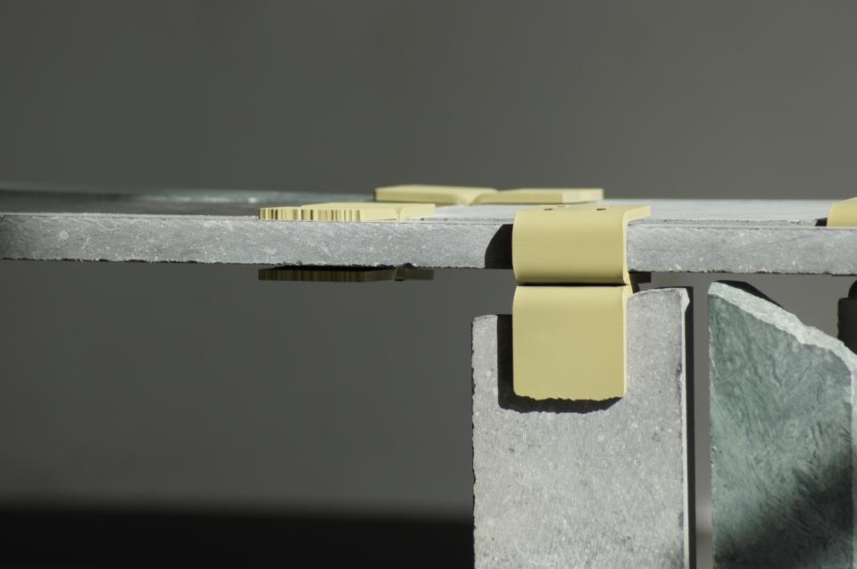 Minimalist table design featuring innovative yellow fasteners with a textured gray stone surface, showcasing Dutch craftsmanship at Design Week 2024.