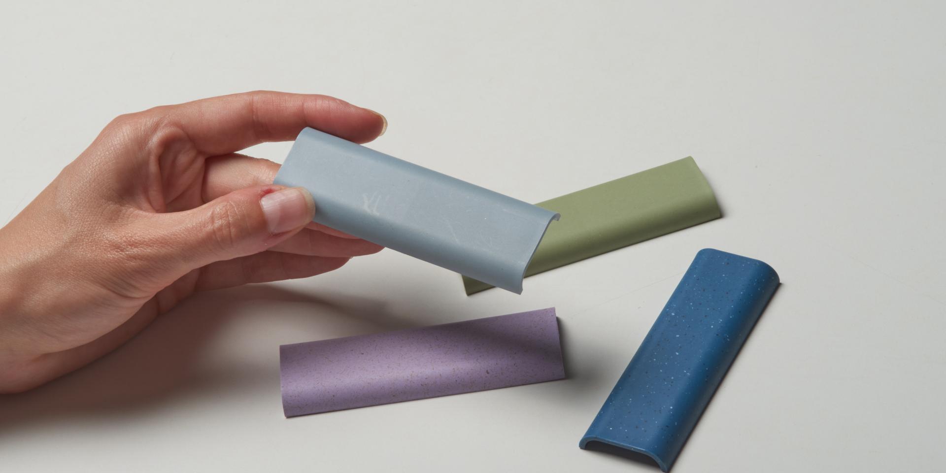 Hand holding a blue CMF material sample, surrounded by various colorful sustainable materials, illustrating luxury and sustainability in design.