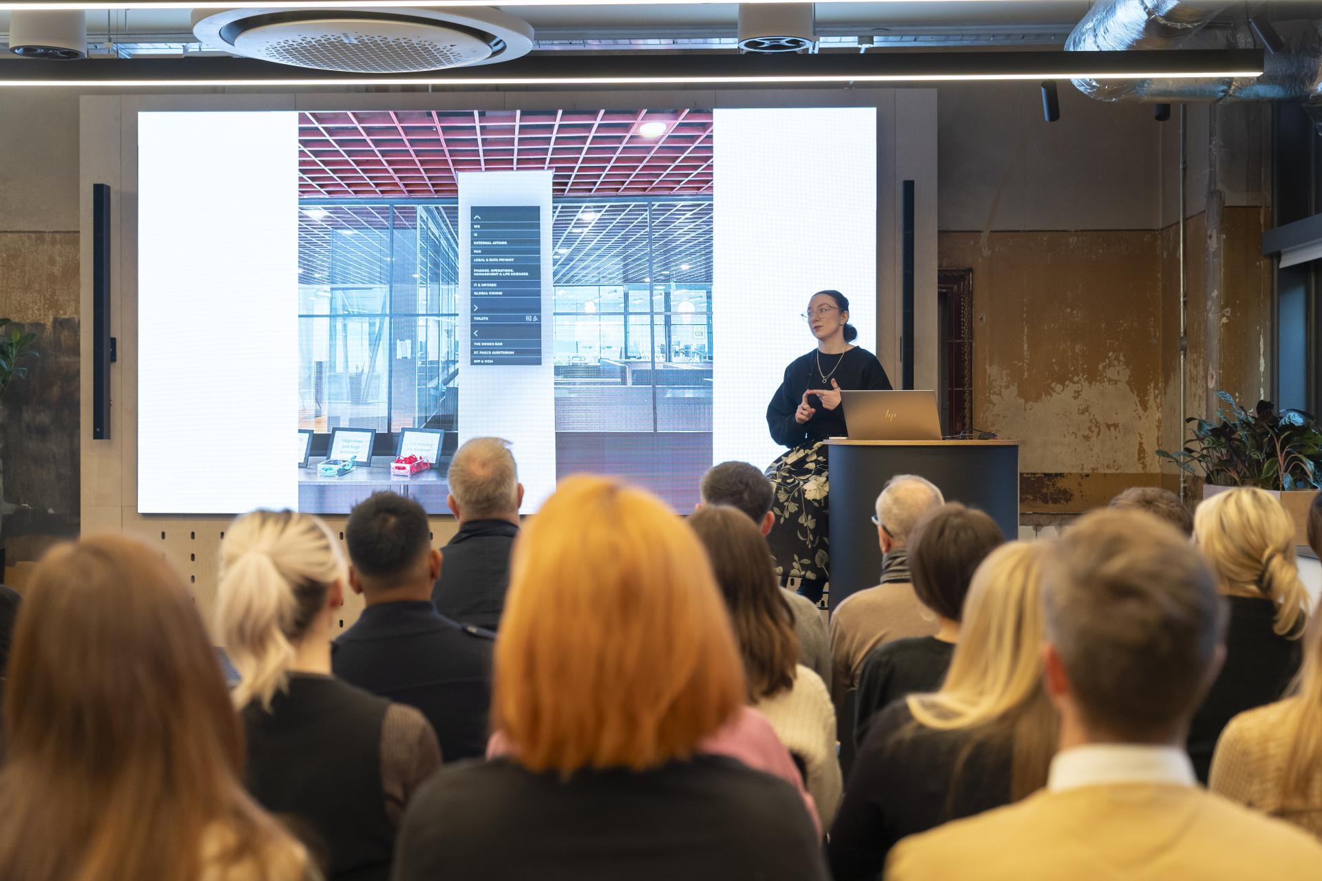 Architect Stephanie Kyle presents on inclusive design for neurodiversity, with a digital display showcasing accessible washroom designs.