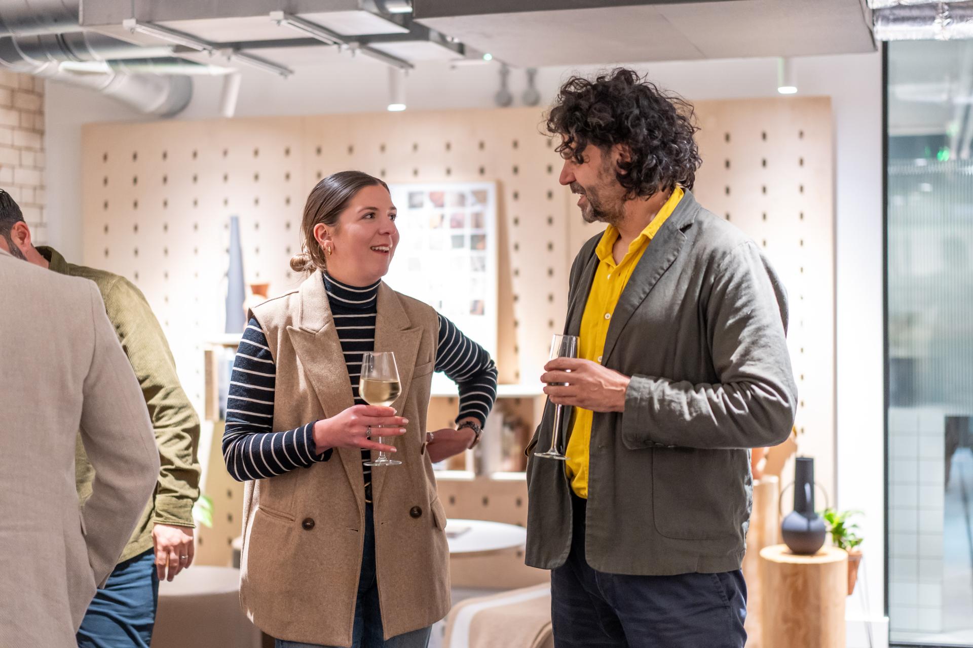Two guests engaging in a conversation at a modern EDI-focused event, holding drinks and dressed in stylish attire.