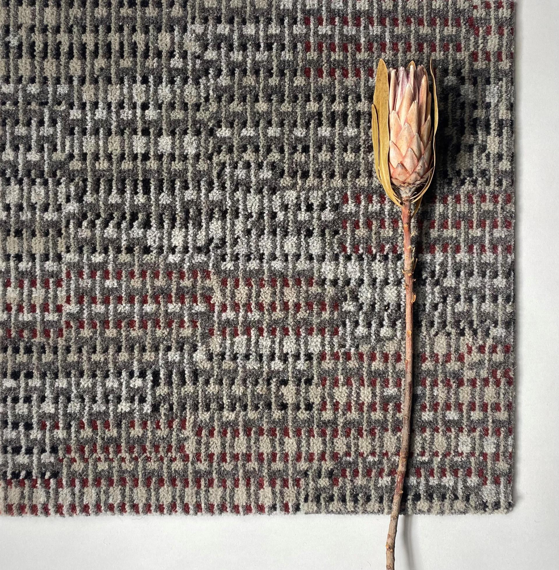 Textured carpet from Newhey's Macramé Collection, adorned with a dried flower, showcasing craft-inspired design elements.