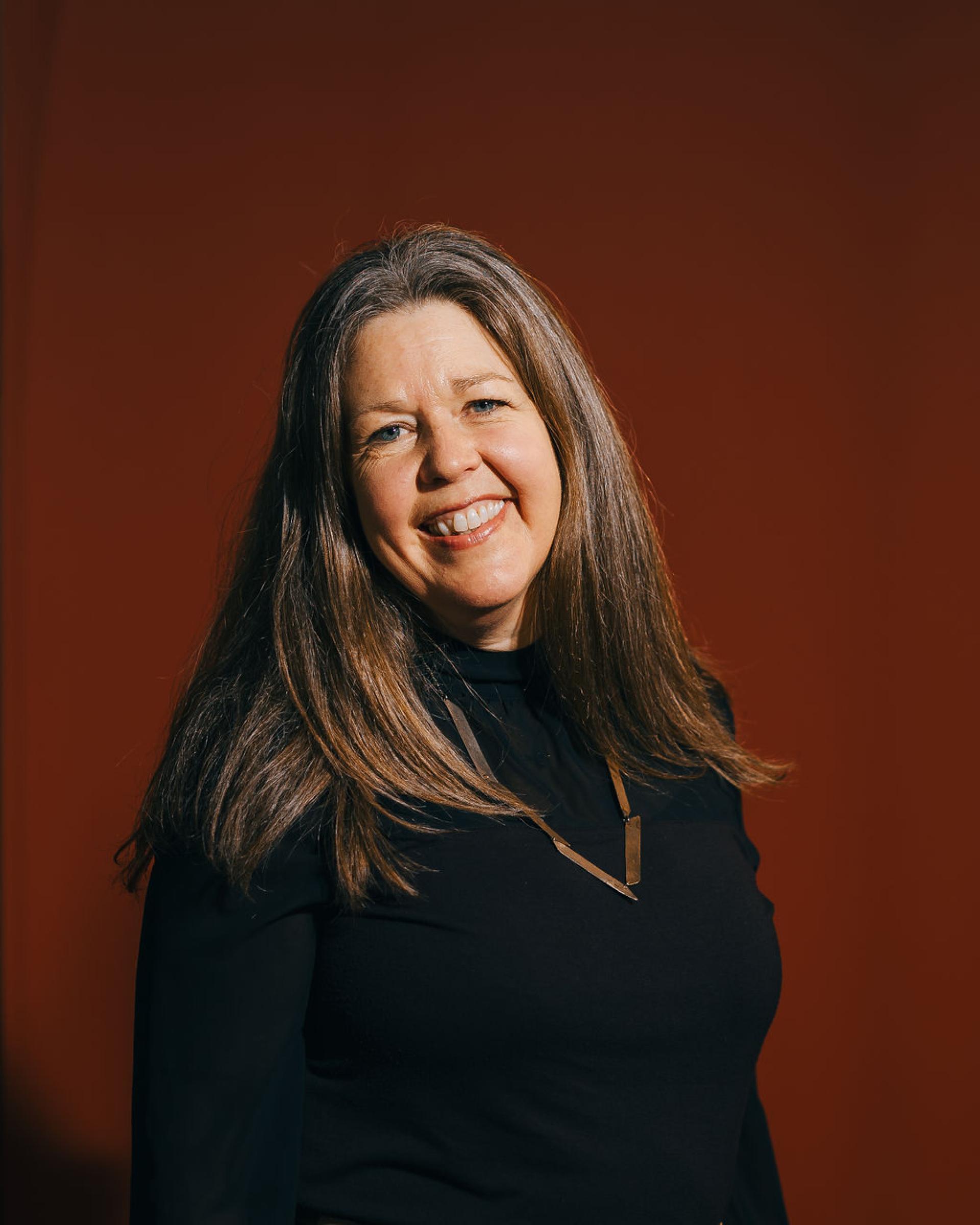Smiling woman in a black top with long hair, representing leadership in biomaterials and sustainability discussions.