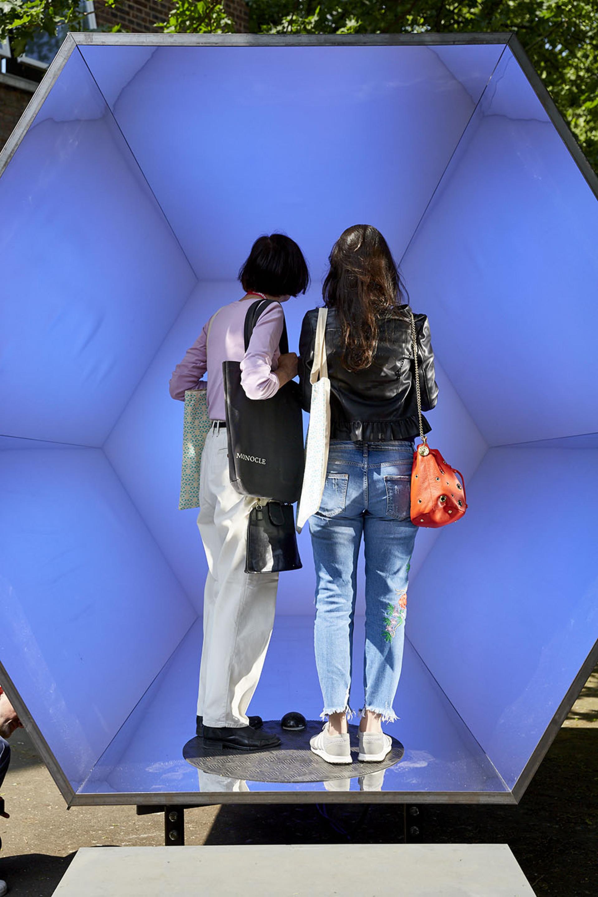 Two women exploring an artistic installation with a blue interior at Clerkenwell Design Week's 10th anniversary celebration.