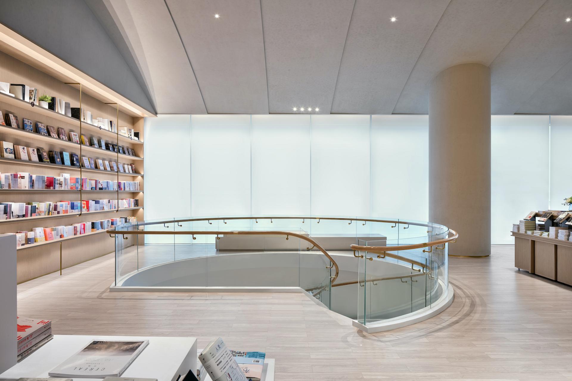 Modern bookstore interior featuring curved glass railing and shelves lined with books, designed by Karv One for Symbiotic Island.