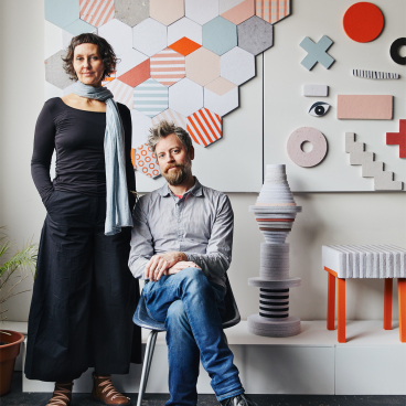 Jasna Sokolovic and Noel O’Connell pose in front of colorful geometric artworks created by their collaborative, Dear Human.