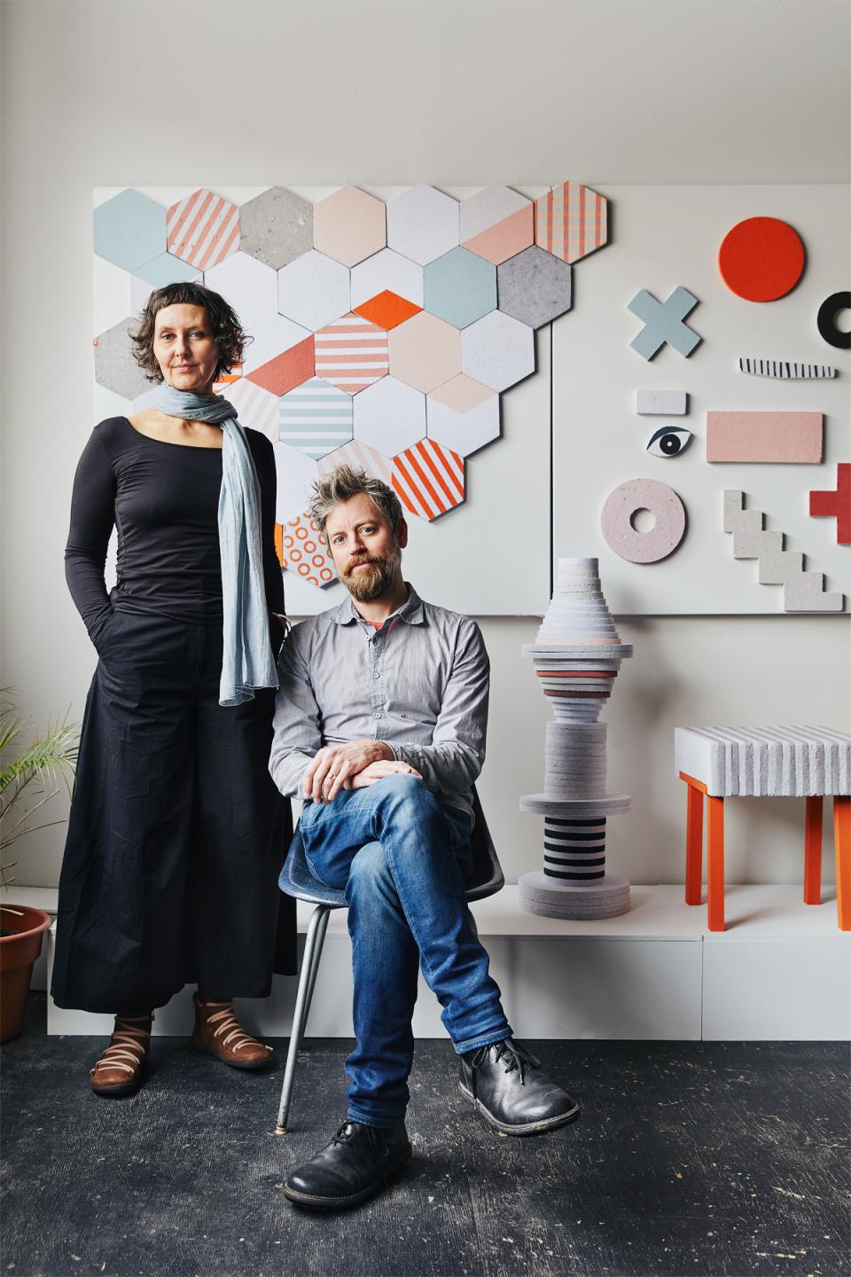 Jasna Sokolovic and Noel O’Connell pose in front of colorful geometric artworks created by their collaborative, Dear Human.