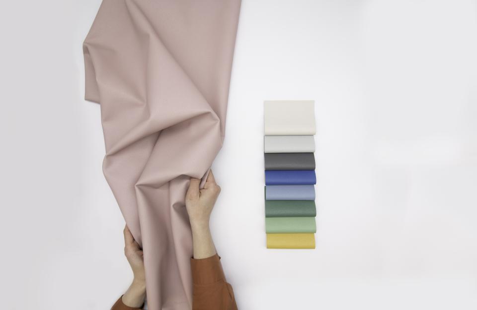 A person holds a soft, recycled performance fabric swatch, showcasing various colors for innovative sustainable design.
