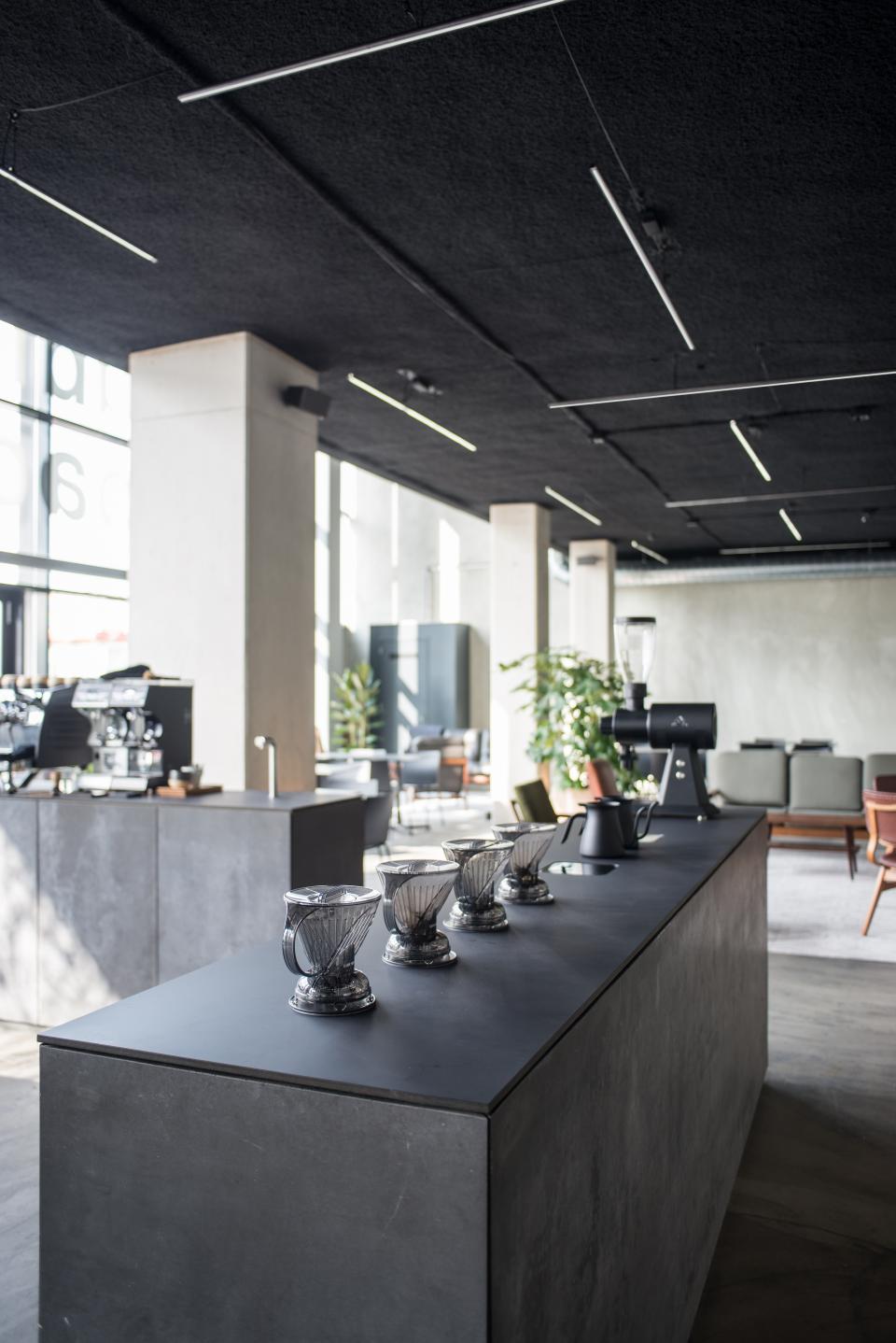 Minimalist café interior at HOP Public Space, featuring sleek surfaces, modern lighting, and brewing equipment setup.