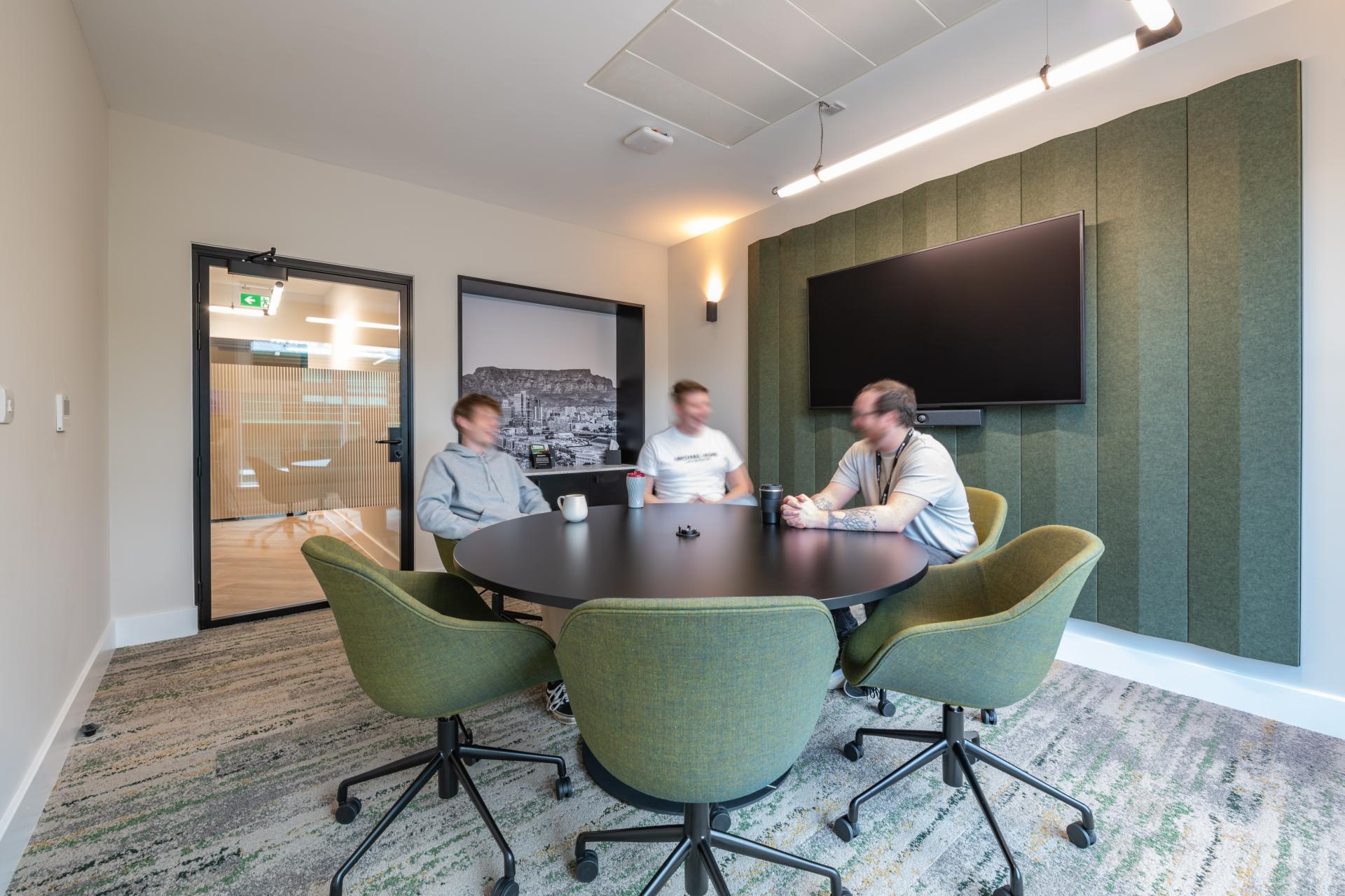 Collaborative meeting space featuring three individuals around a modern round table, reflecting the FinTech workplace design by iDEA.