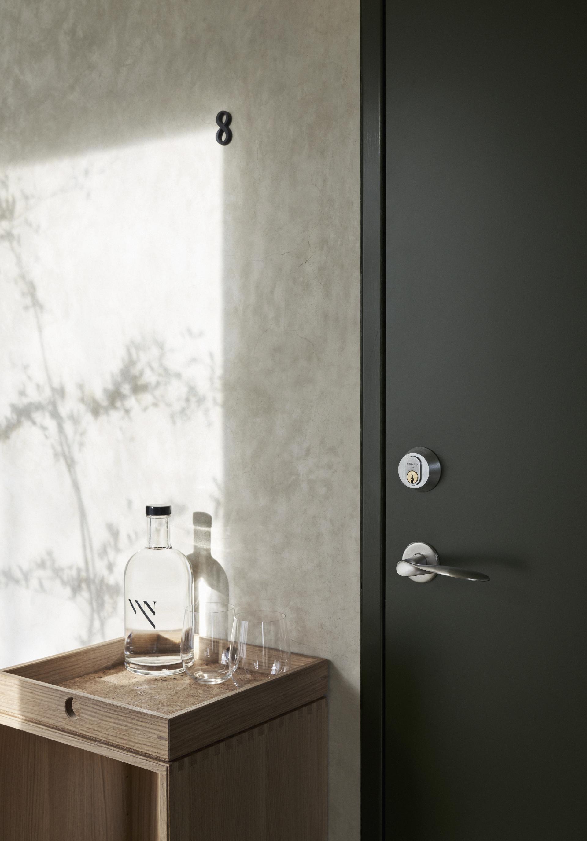 Elegant entrance with wooden storage, bottle, and glasses, showcasing Arne Jacobsen and Knud Holscher design at Vyn, Sweden.