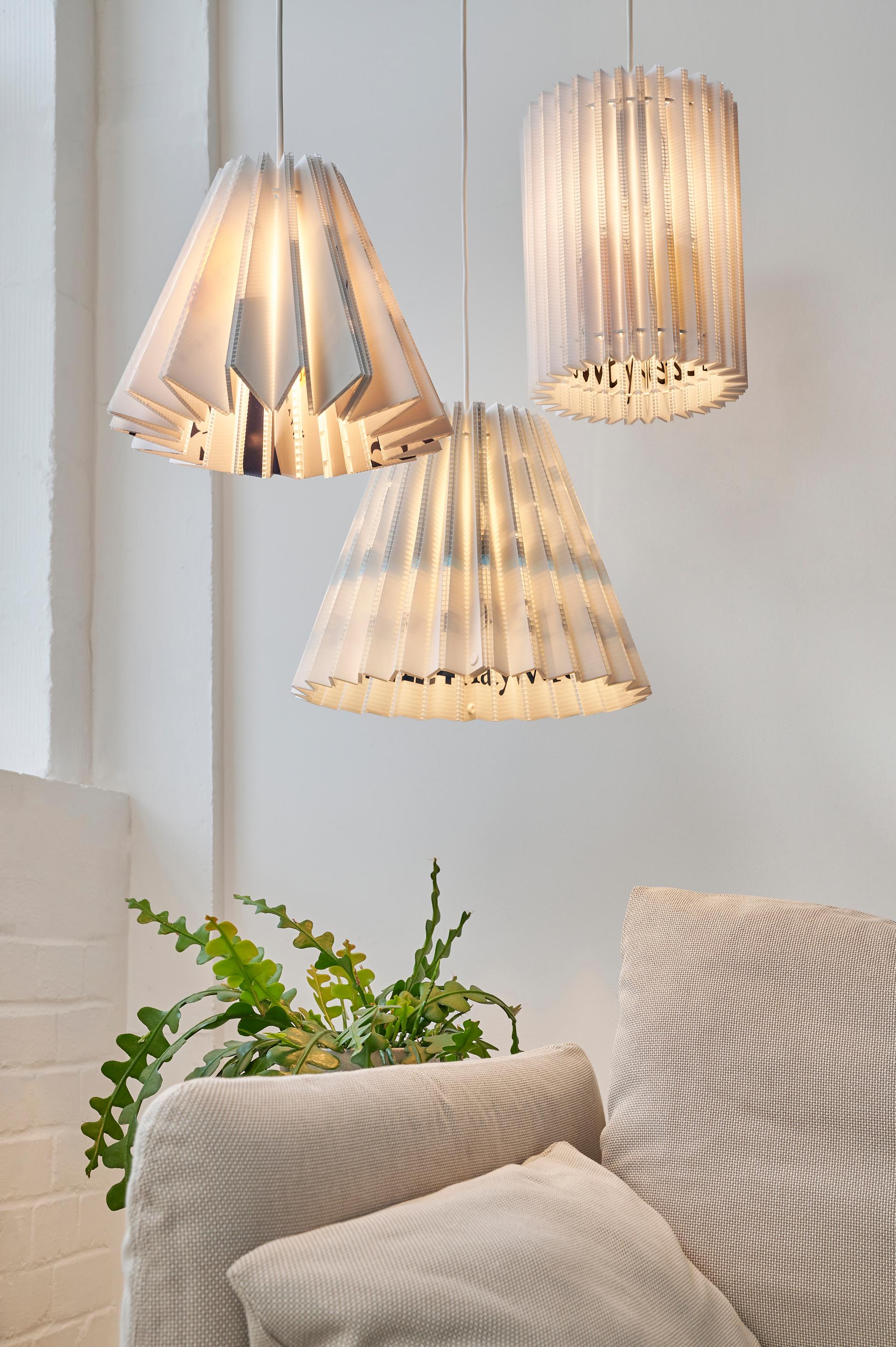 Sustainable sculptural lampshades from Tabitha Bargh's Poly collection hang elegantly above a cozy sofa with greenery.