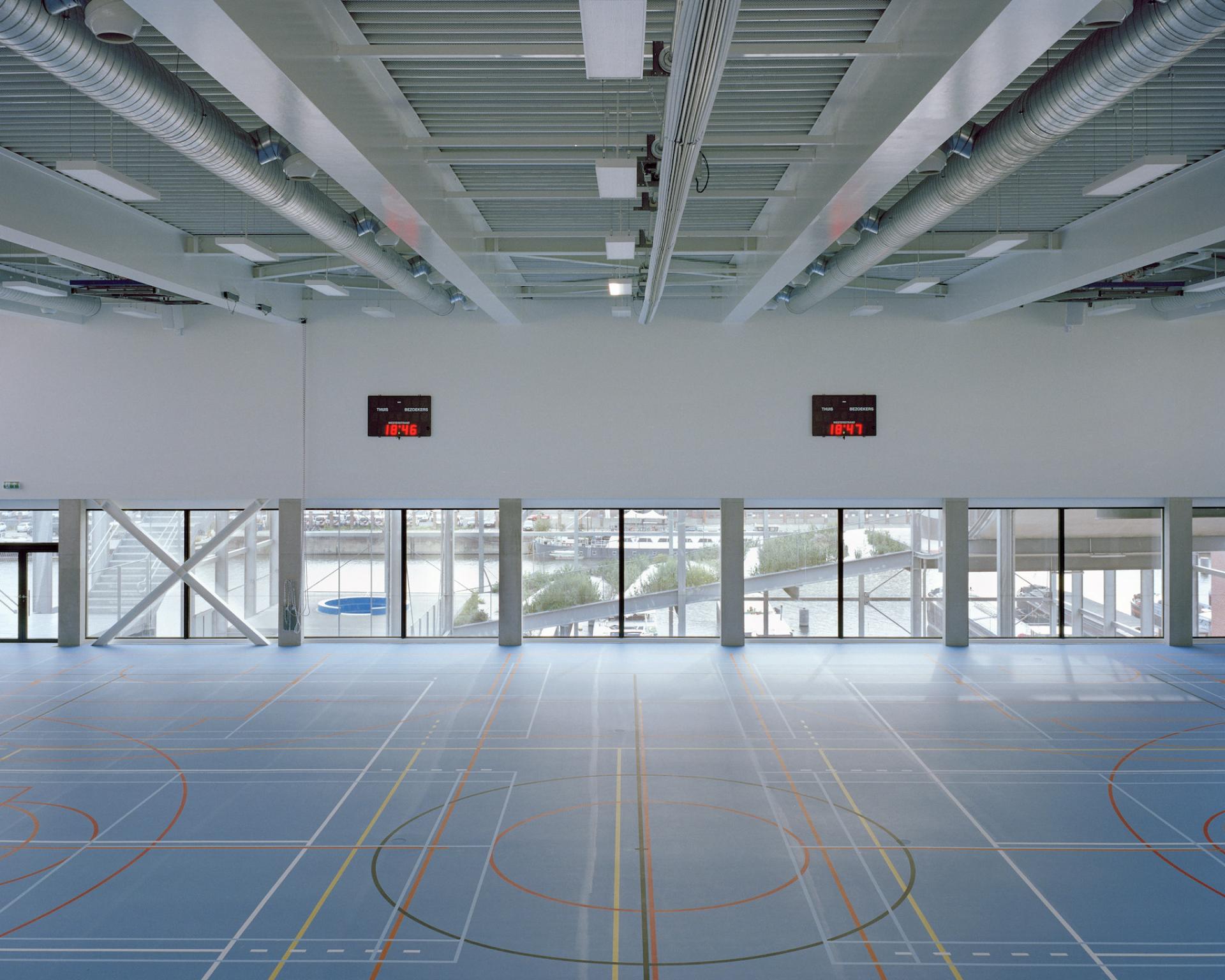 Spacious multipurpose sports hall in Harbourside school featuring a hardwood floor, large windows, and digital scoreboards.
