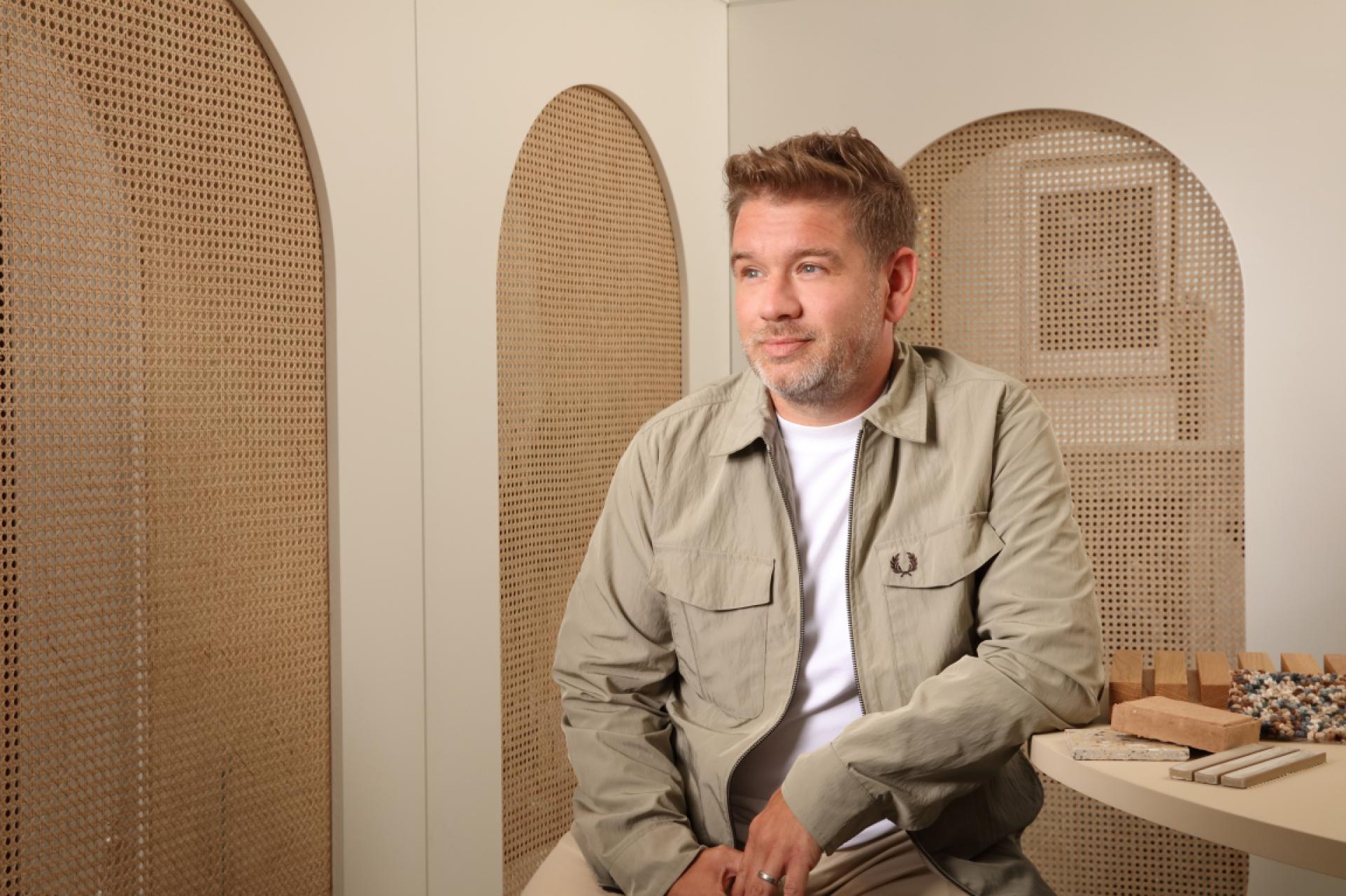 Designer seated in a modern, minimalistic space featuring textured walls and samples of materials for innovative projects.