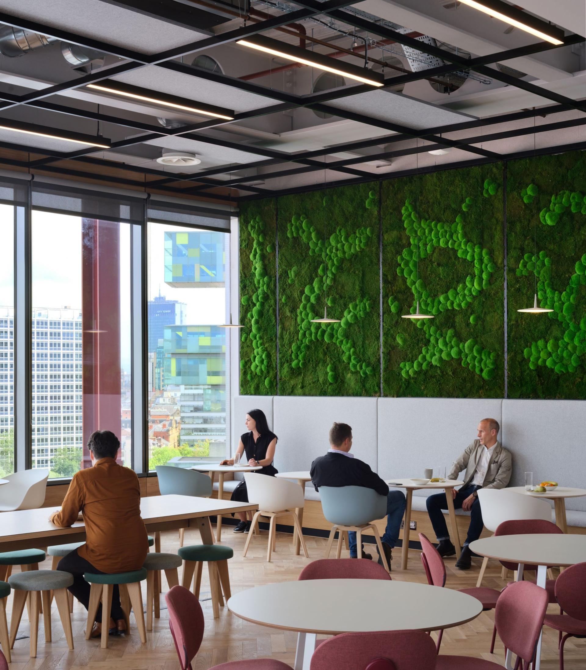 Modern office with green moss wall, featuring professionals engaged in discussion and collaboration in a vibrant workspace.