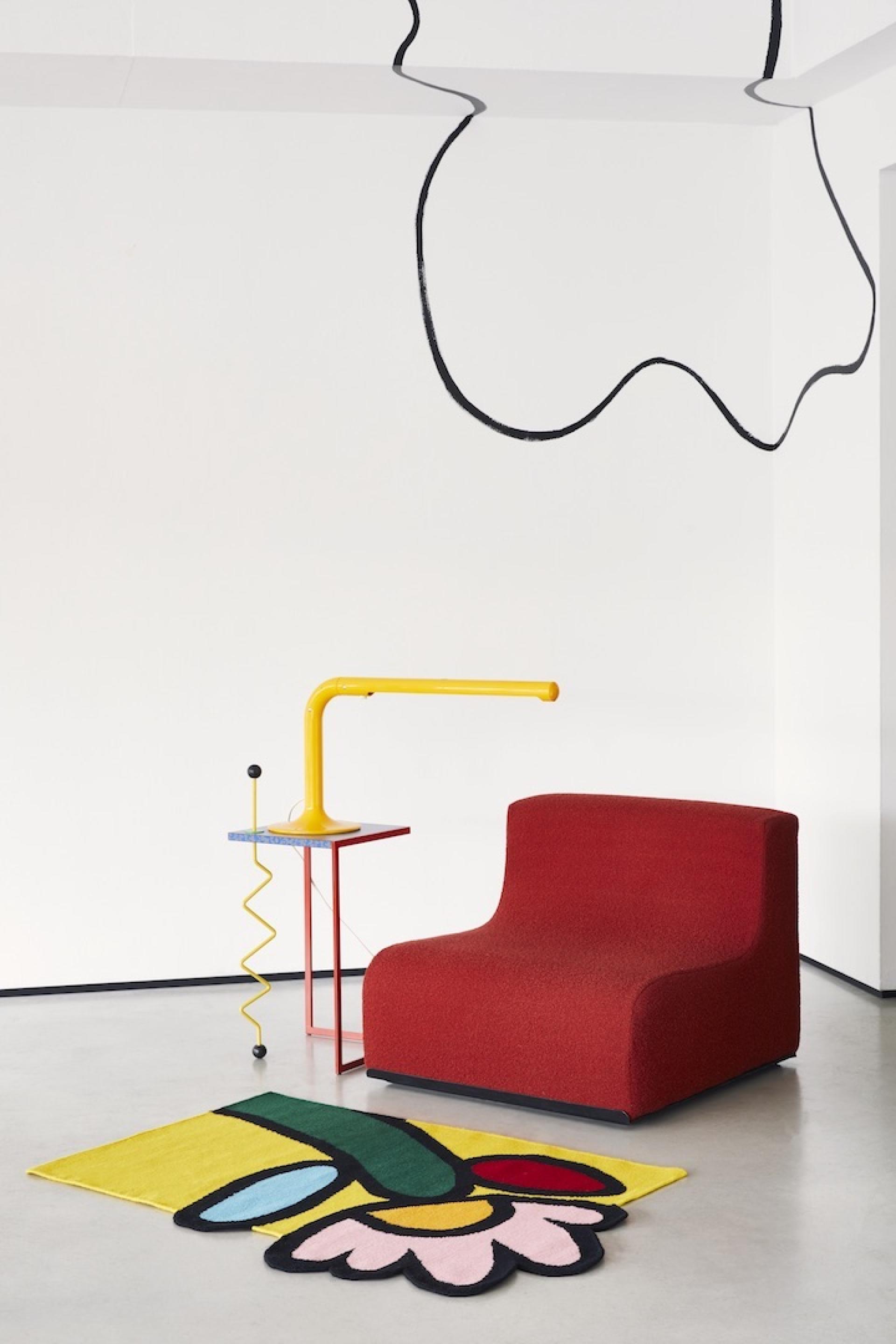 Colorful modern furniture featuring a red chair, yellow lamp, and artistic rug, showcasing the collaboration with John Booth.