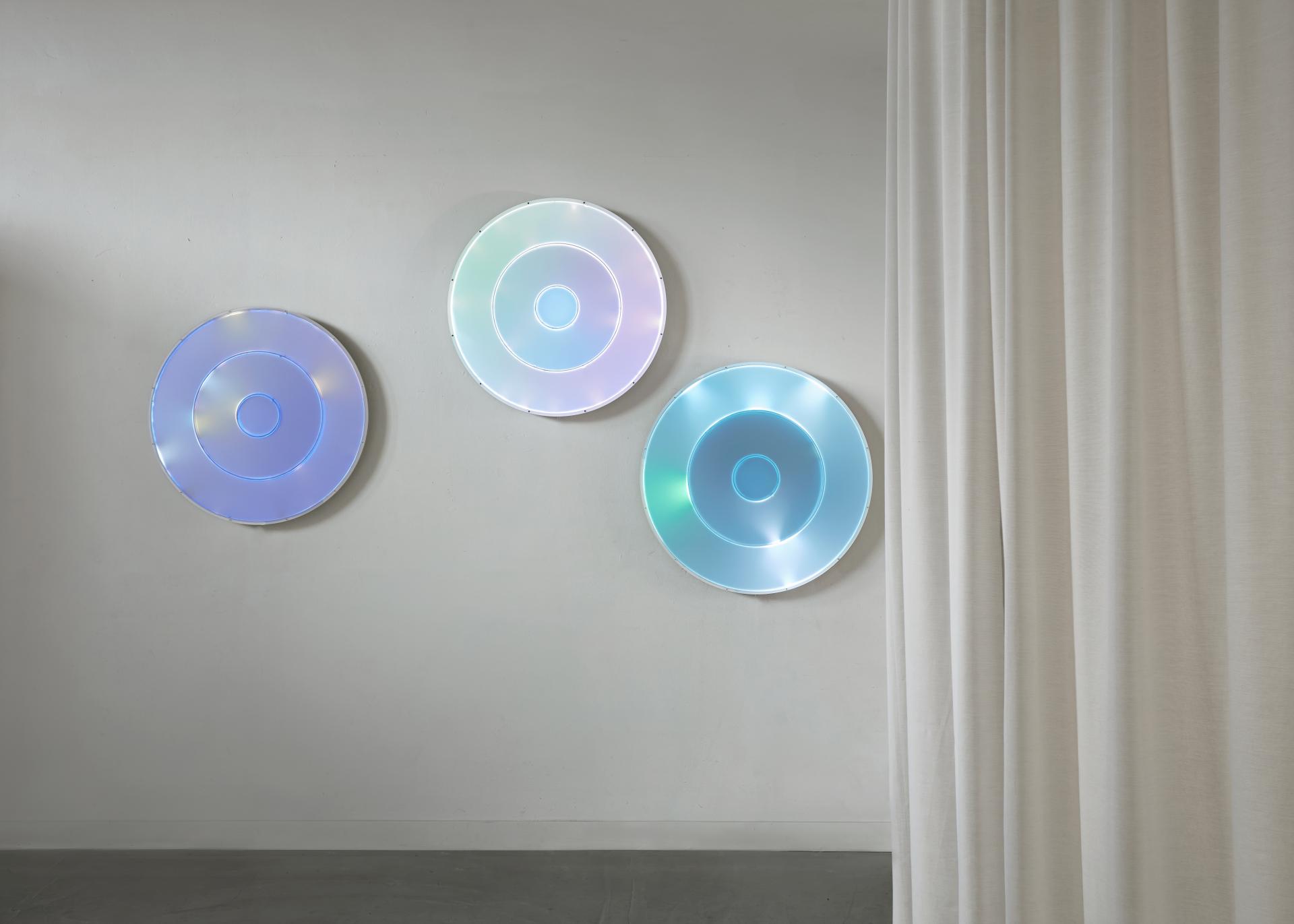 Three illuminated circular artworks on a wall, showcasing biotechnological design elements for restorative interior spaces.