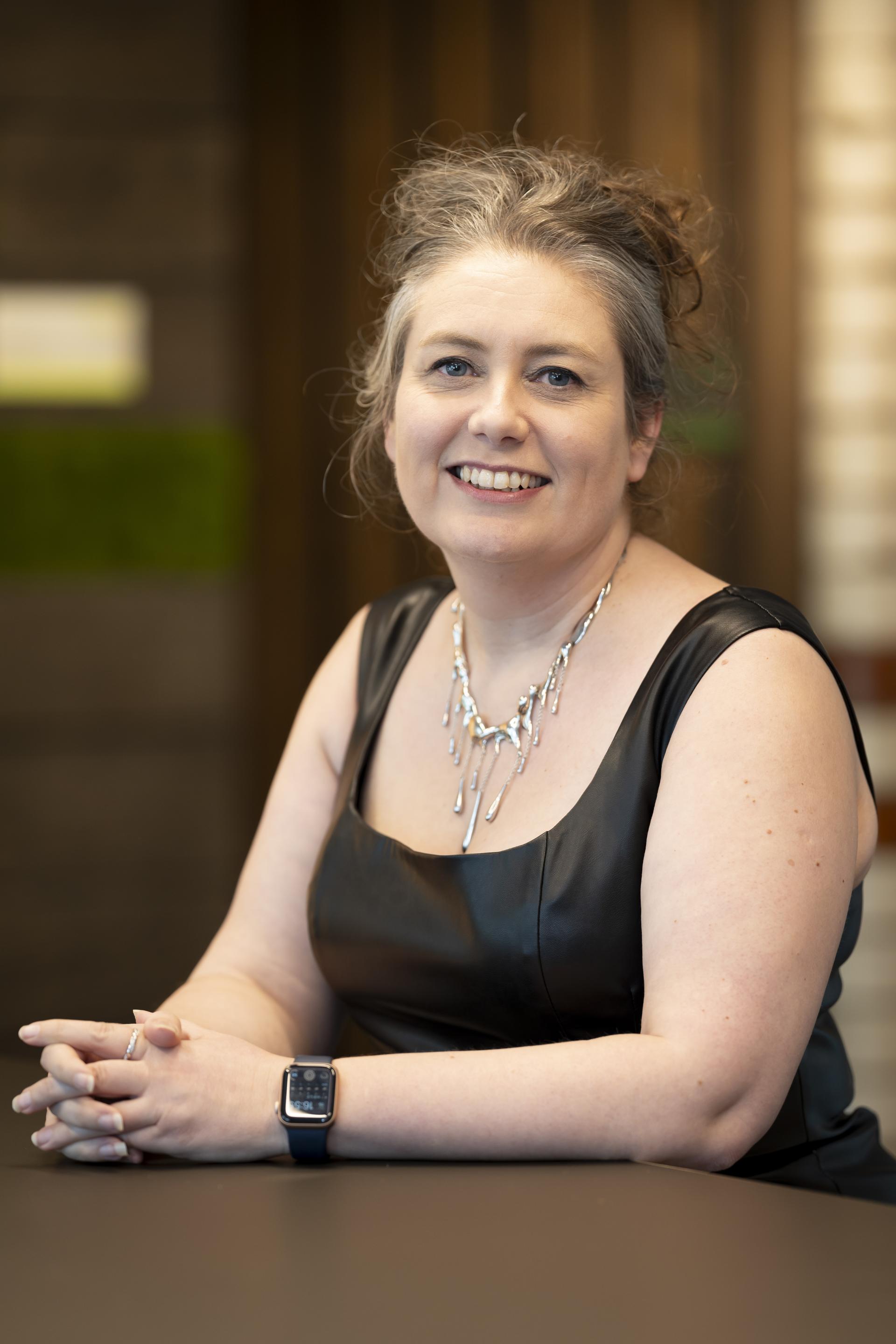 Senior designer discussing technology's role in sustainable design, wearing a stylish black top and modern jewelry.