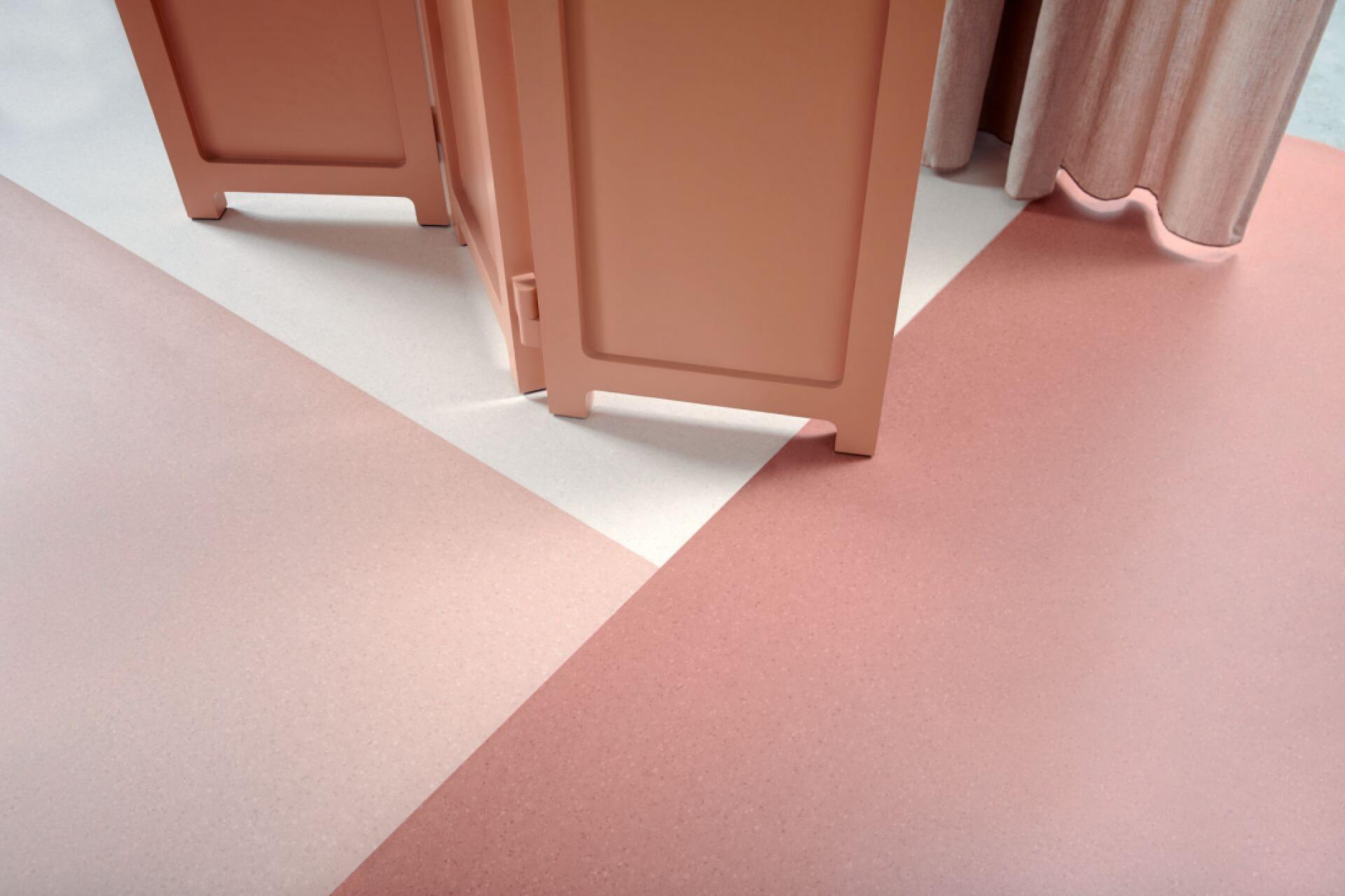 Textured flooring in muted pink tones complements a partition and soft fabric curtains in a contemporary studio setting.