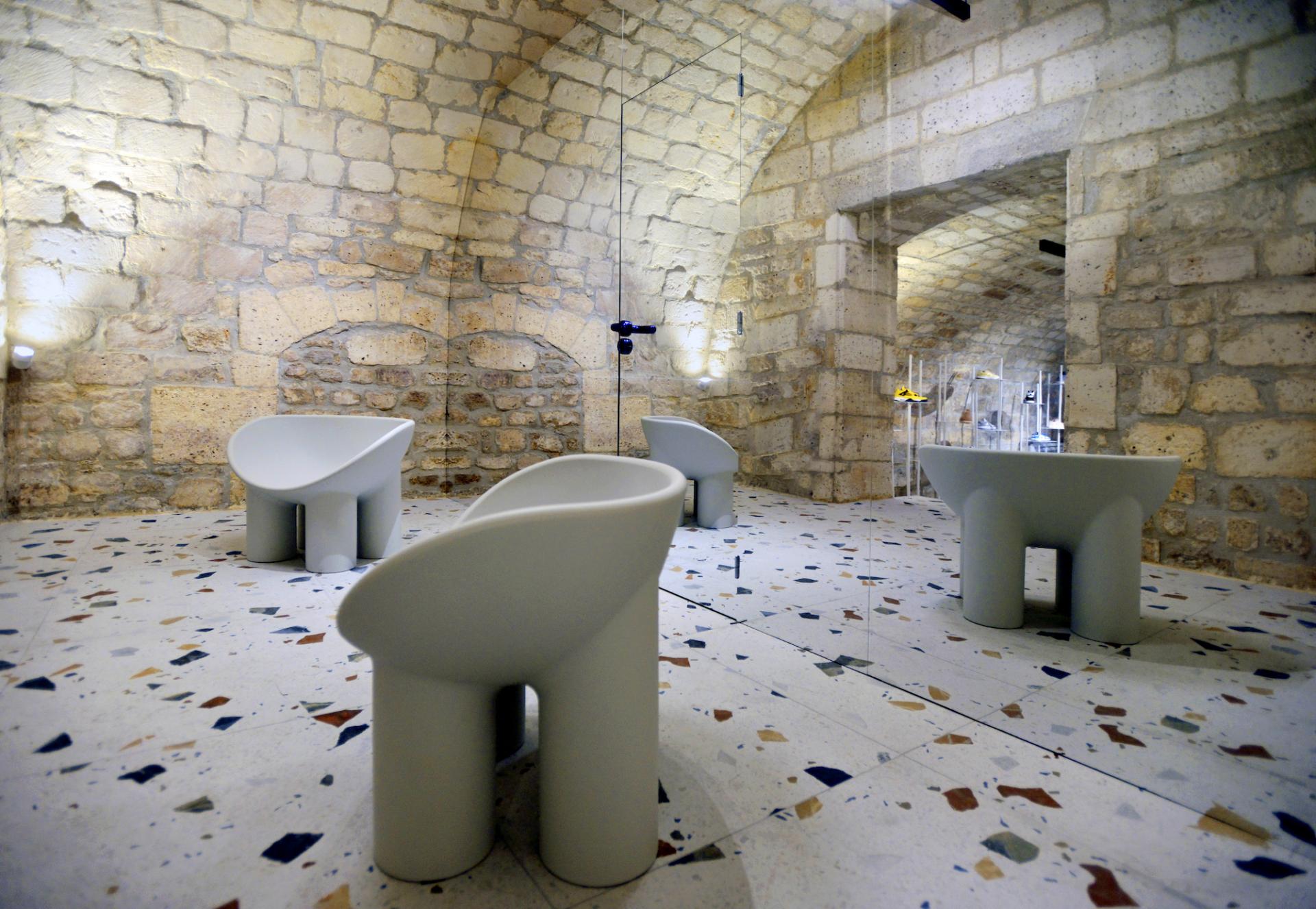 Modern minimalist chairs in a stone-walled concept store, showcasing a blend of futuristic design and electric blue accents.