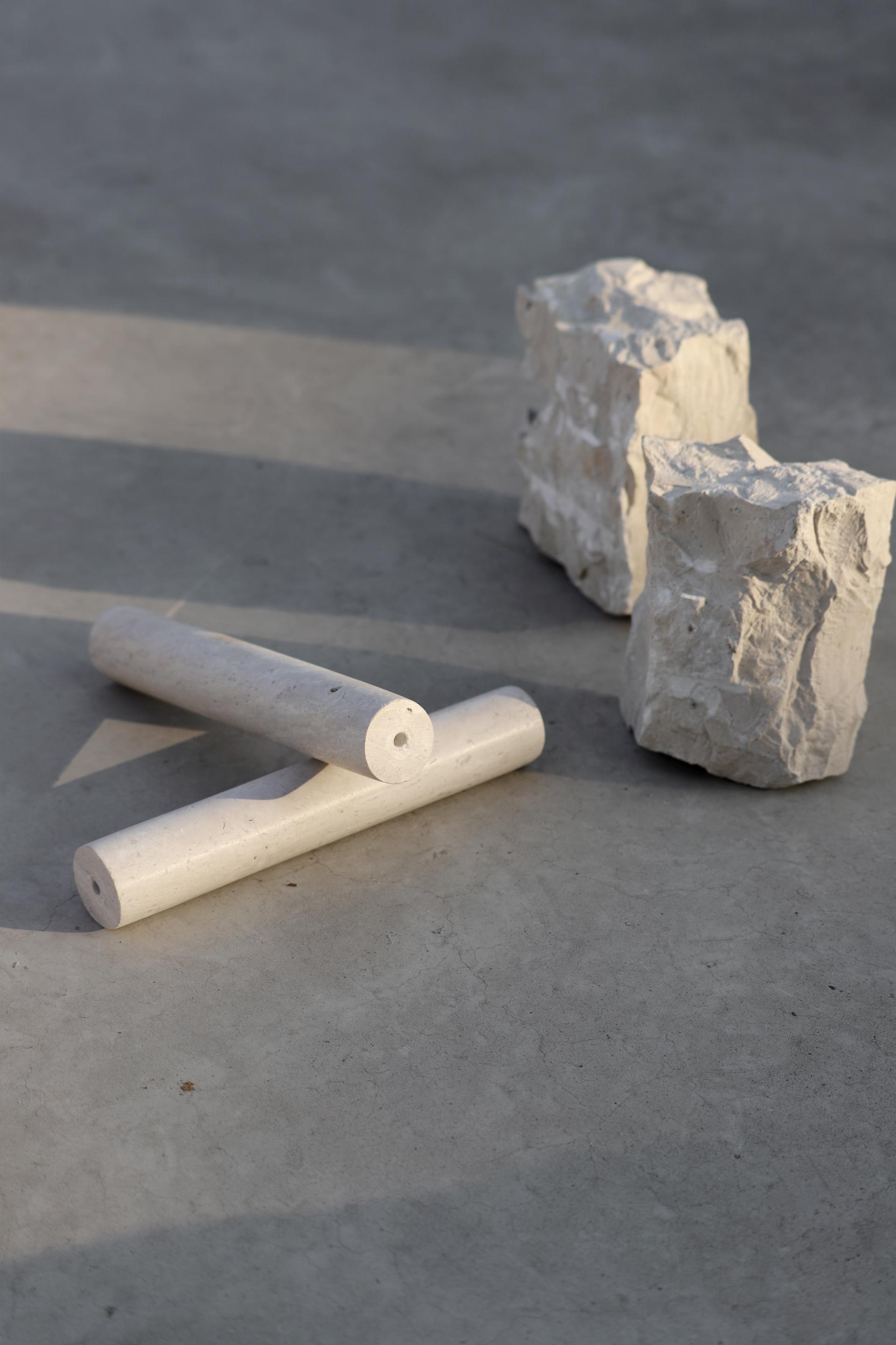Two textured stone pieces alongside white cylindrical forms, showcasing the new Meta finishes by studio davidpompa.