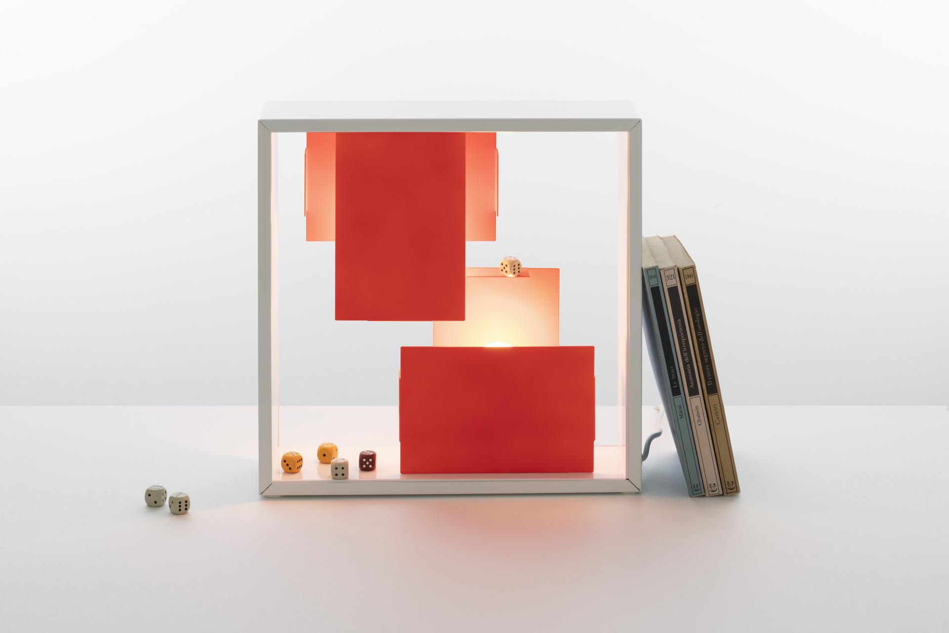 New bi-colour Artemide Tolomeo Micro lamp showcasing vibrant red shades, alongside books and decorative dice.