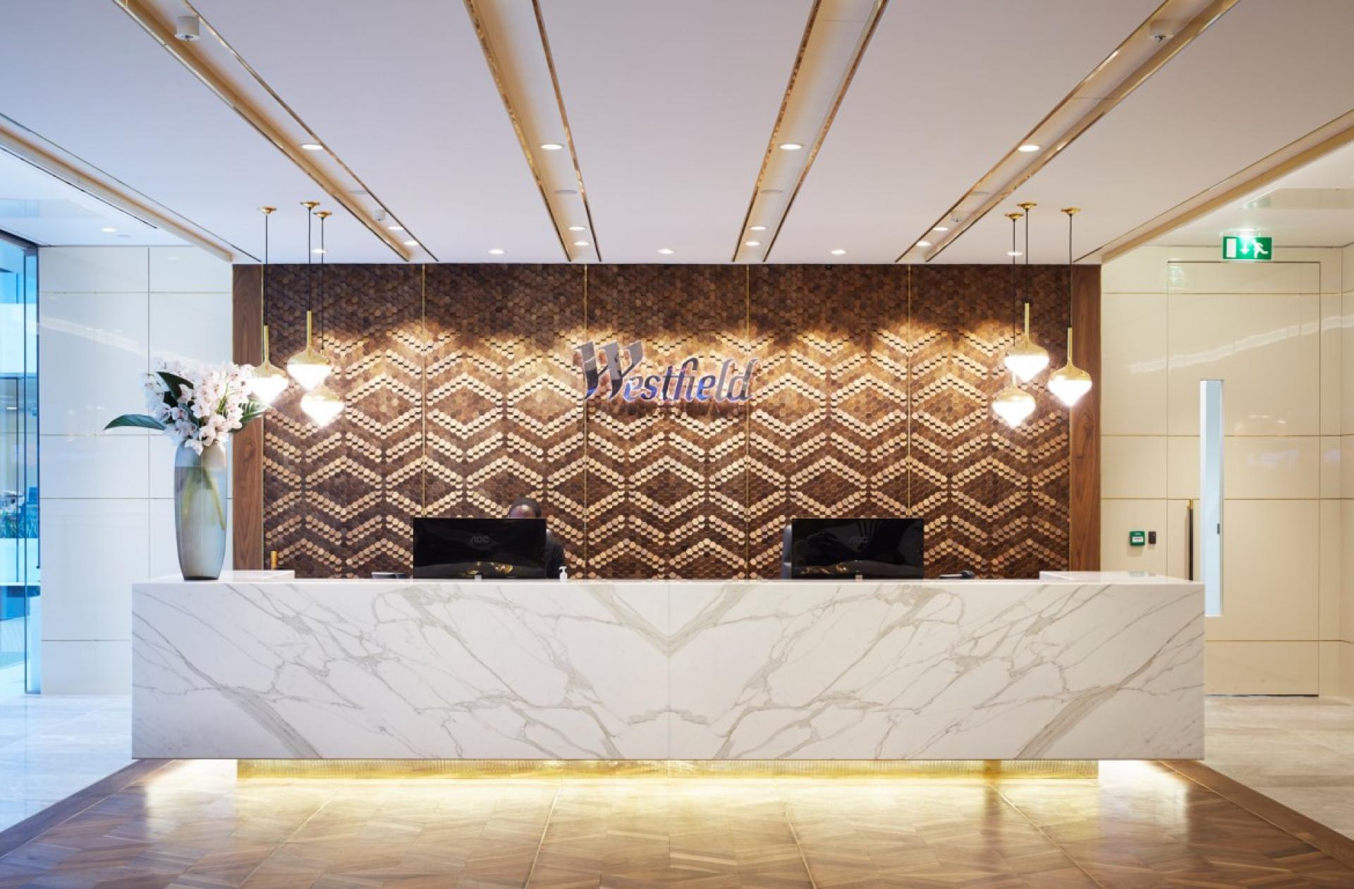 Contemporary reception area featuring a geometric wooden wall design and elegant lighting at Westfield, showcasing innovative materiality.
