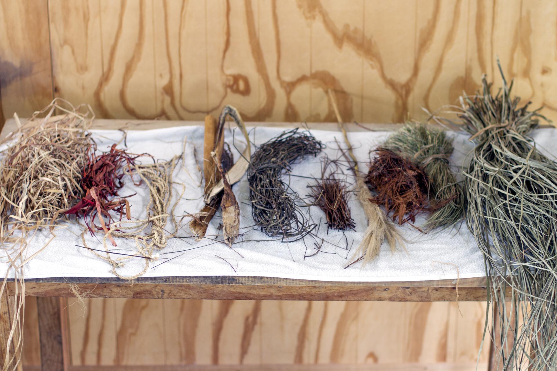 Various natural materials including dried grasses and fibers used in crafting Carolina Palombo’s Tutura chair on a wooden table.