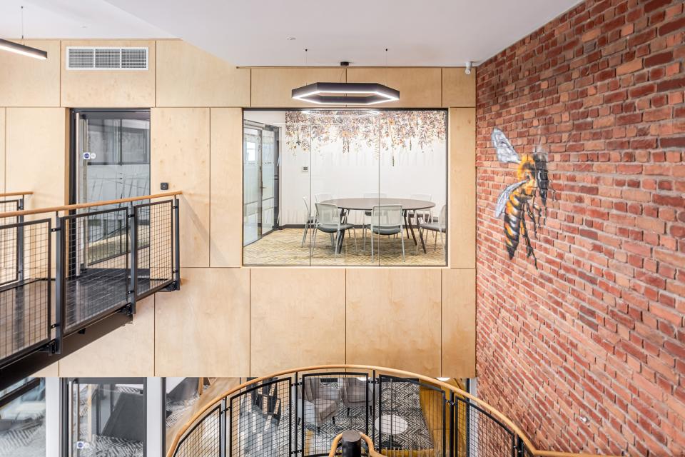 Modern collaborative workspace at The Bee House, featuring a meeting room and artistic bee mural on exposed brick wall.
