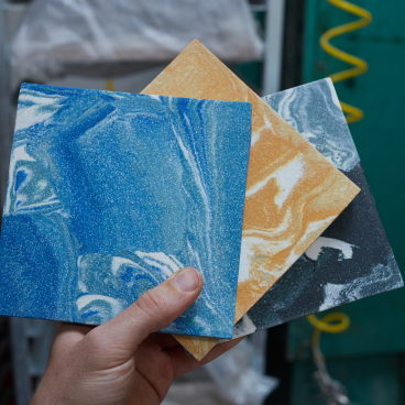 Hand holding three colorful encaustic tiles showcasing vibrant blue, yellow, and black marbled designs from Granby Workshop.