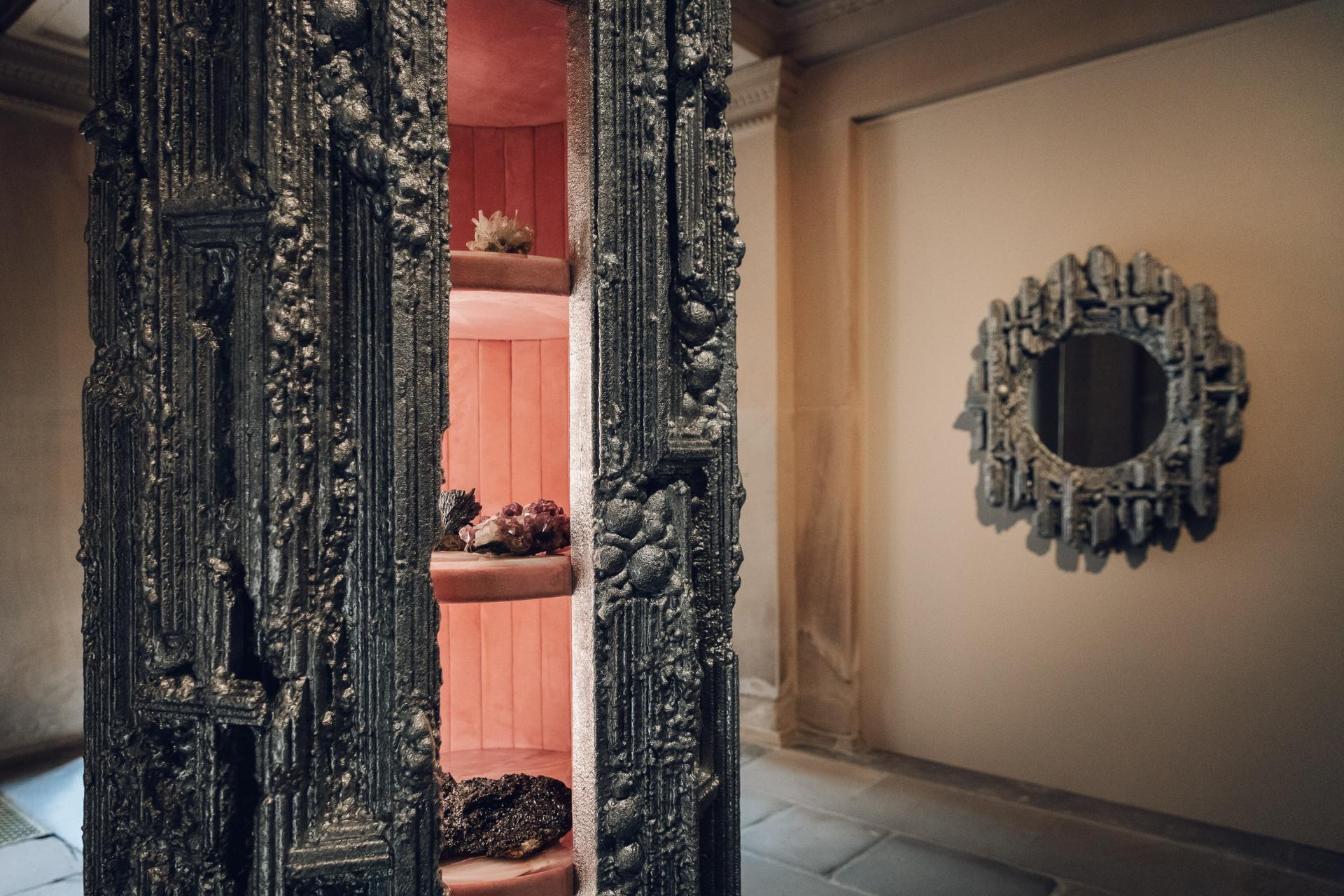 Intricately designed display cabinet showcasing natural elements, with an ornate mirror reflecting Chatsworth House's artistic heritage.