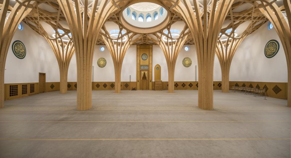 Spacious interior of Cambridge Central Mosque featuring wooden arches, decorative wall art, and a sacred prayer area.