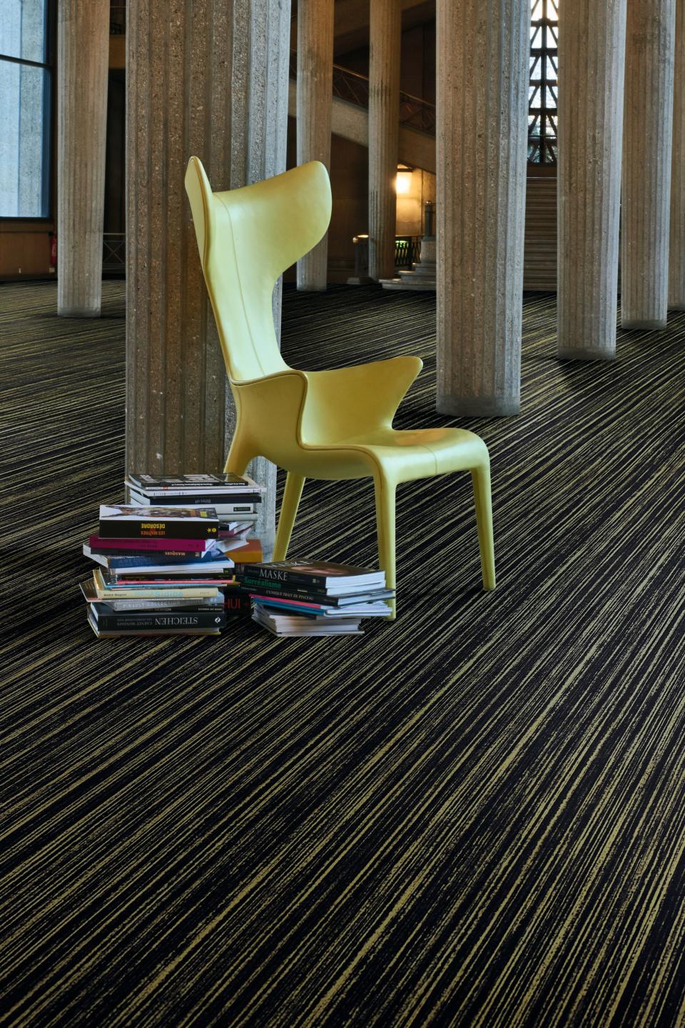Yellow designer chair beside a stack of books on striking striped Flotex flooring from Forbo's Starck collection.