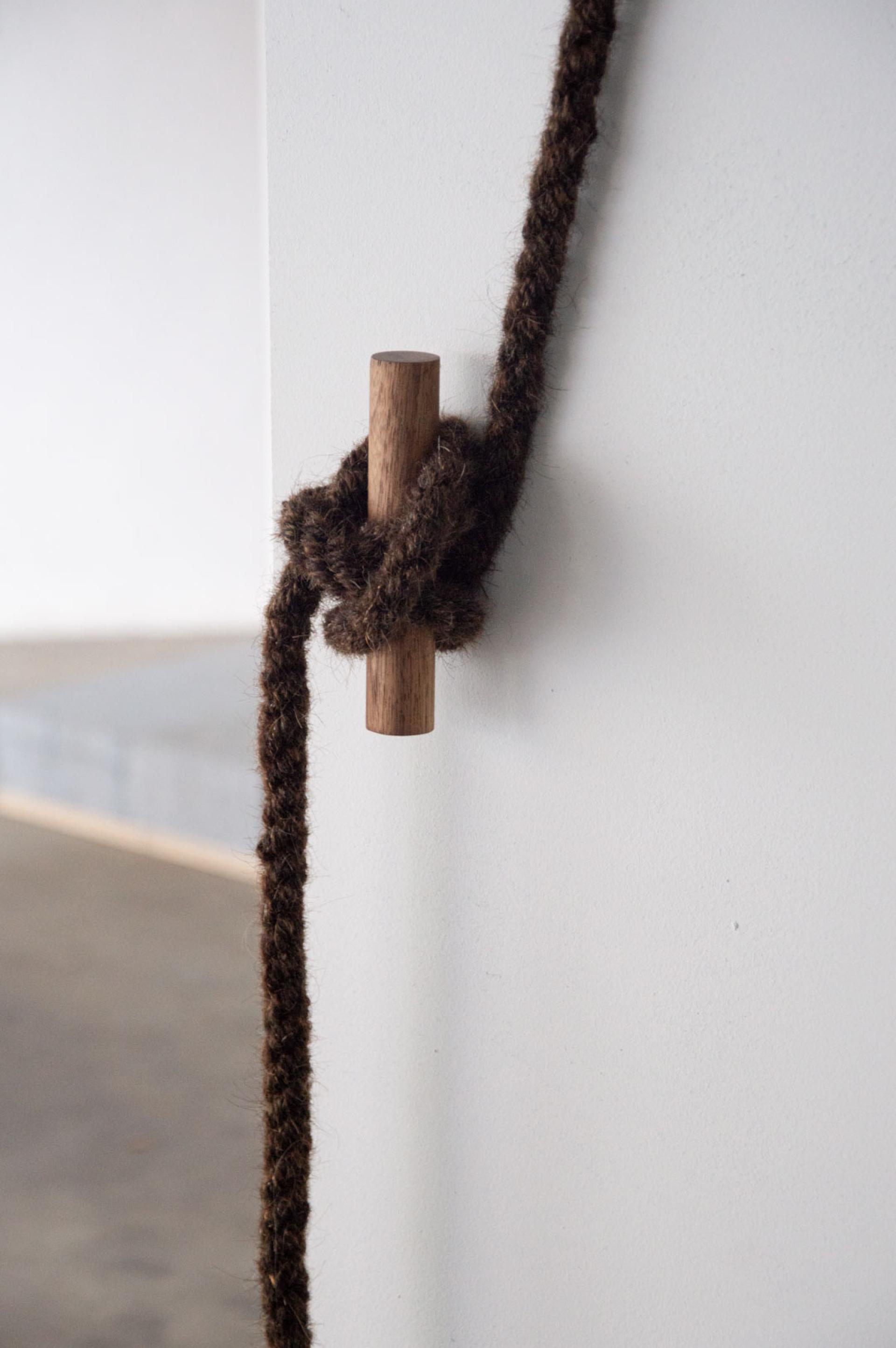 Knot made from natural fiber rope surrounding a wooden post against a minimalist wall, illustrating sustainable design.