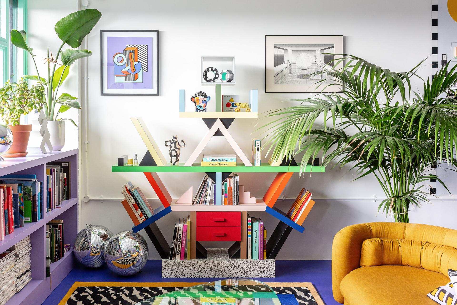 Brightly colored bookshelf featuring geometric designs, art pieces, and plants in Camille Walala's creatively transformed studio space.