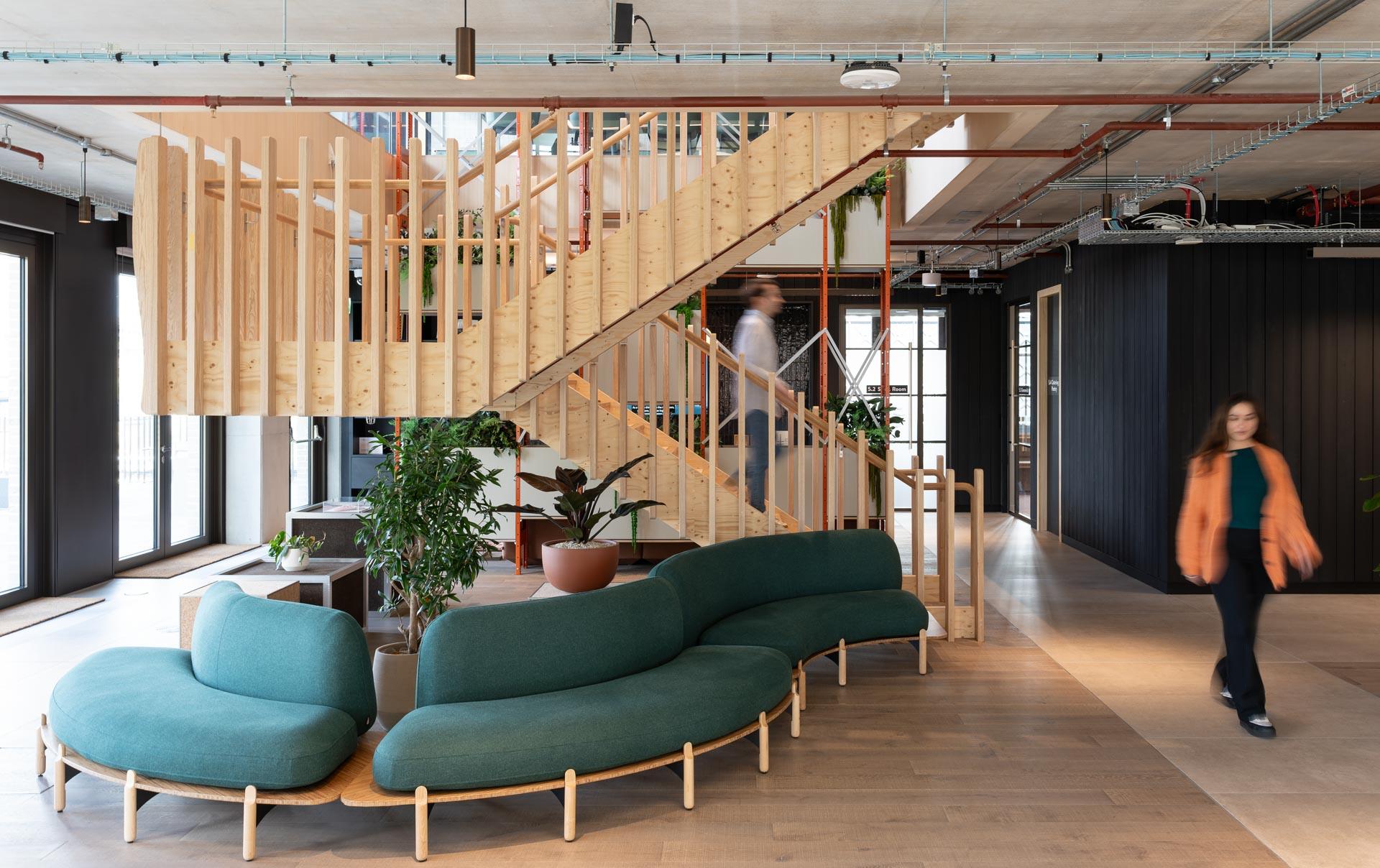 Contemporary workspace featuring a wooden staircase, green seating, and plants, highlighting design for neurodiversity and purposeful impact.
