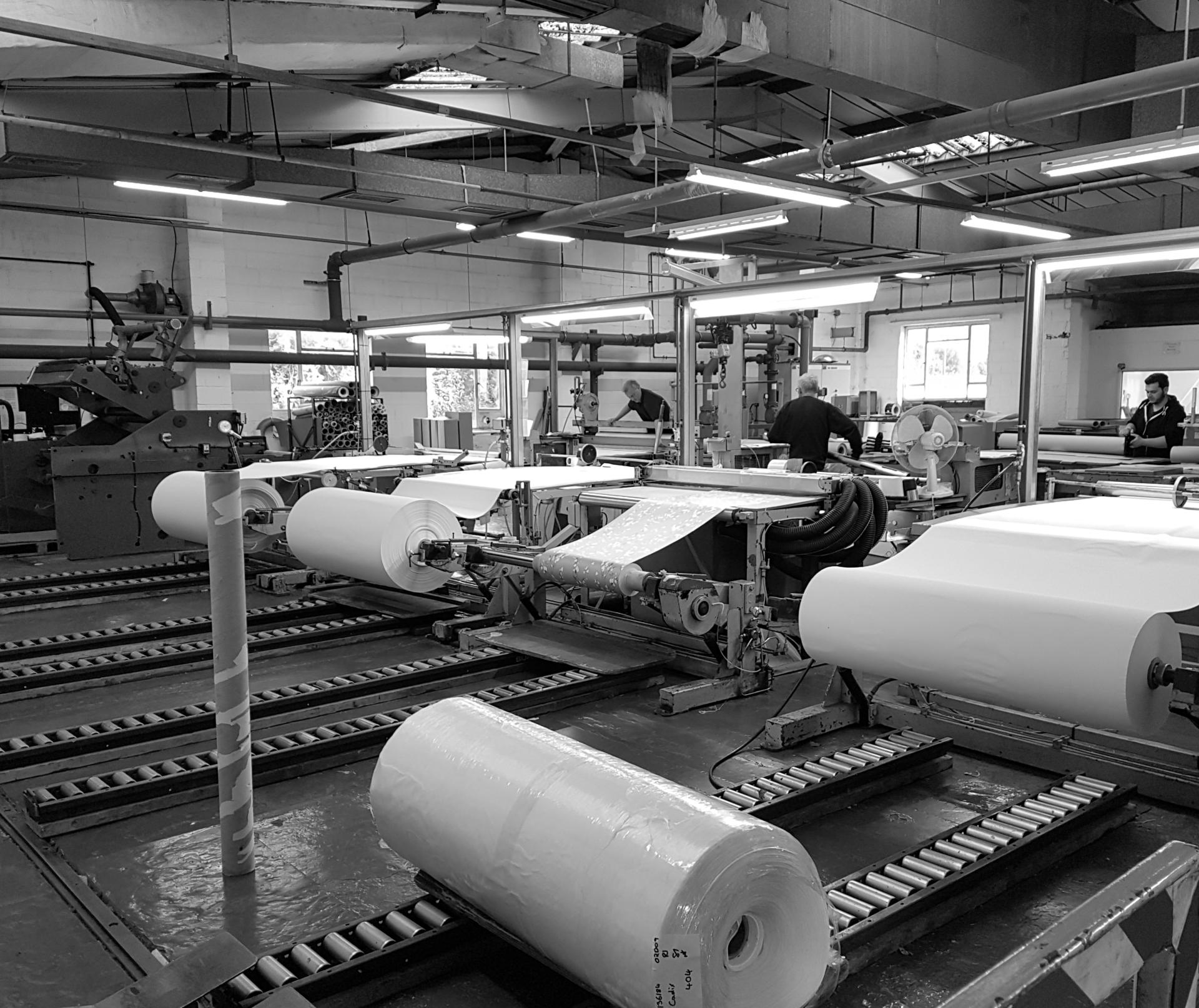 Manufacturing area of Muraspec in Kent, featuring rolls of wallpaper and workers in a production facility.