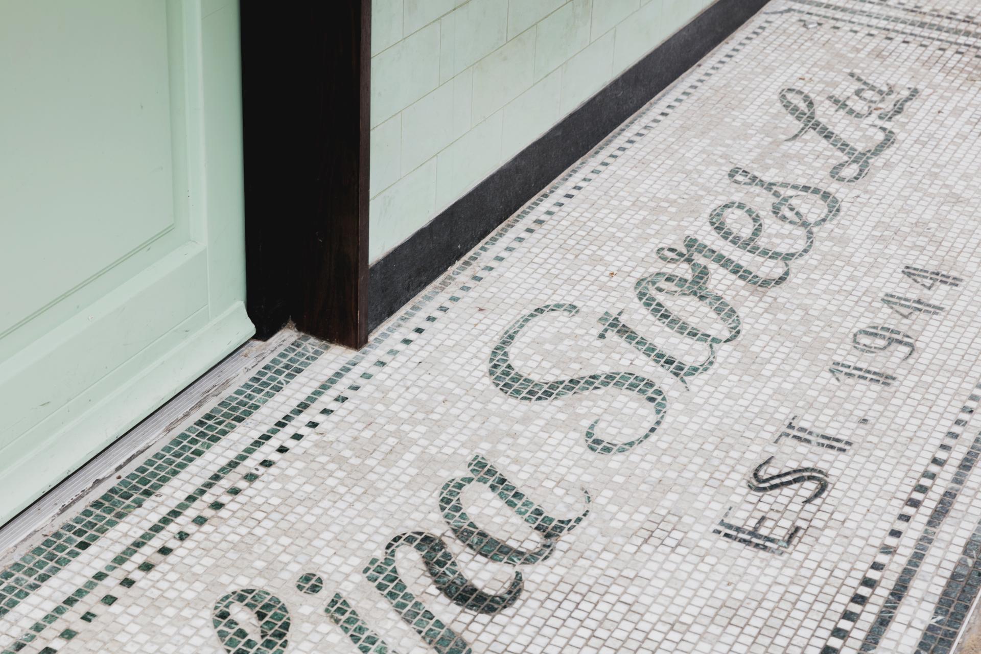 Mosaic floor detail featuring "Lina Stores Ltd" and green accents, showcasing Art Deco design in the Soho restaurant.