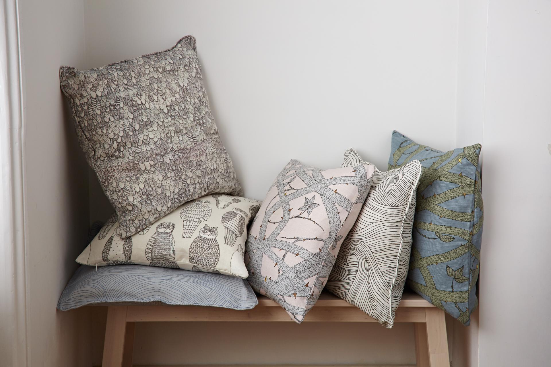 Decorative pillows featuring nature-inspired patterns, showcasing designs with owls, branches, and floral motifs by designer Abigail Edwards.