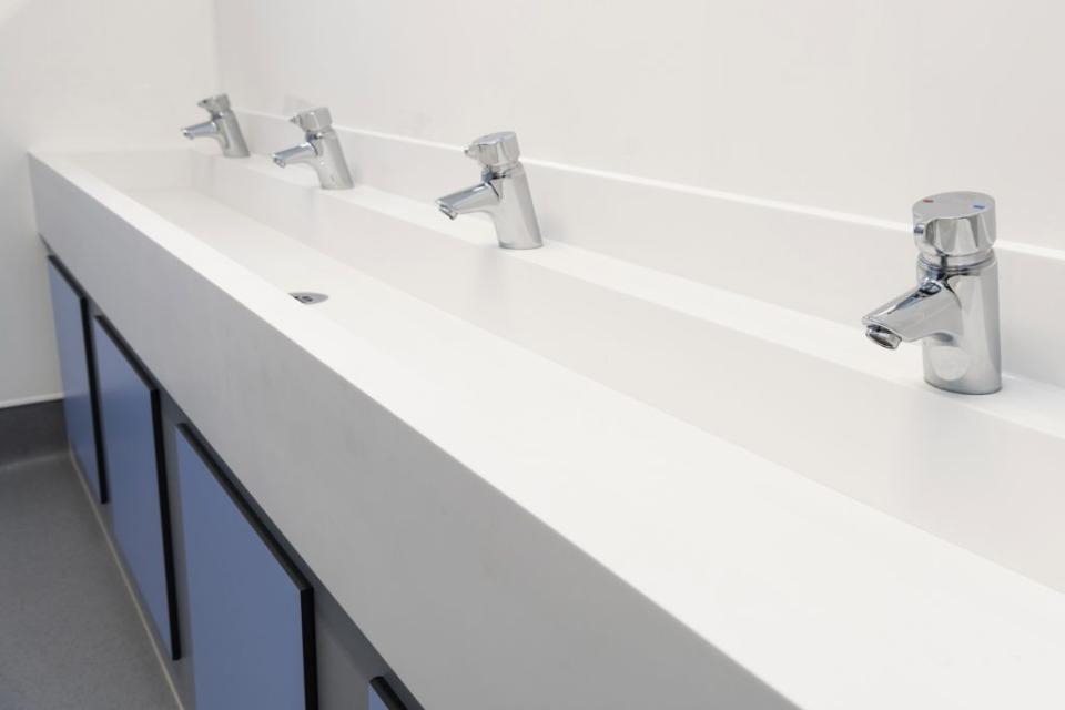 Modern washbasin design featuring four chrome taps and sleek white countertop in an inclusive school washroom.