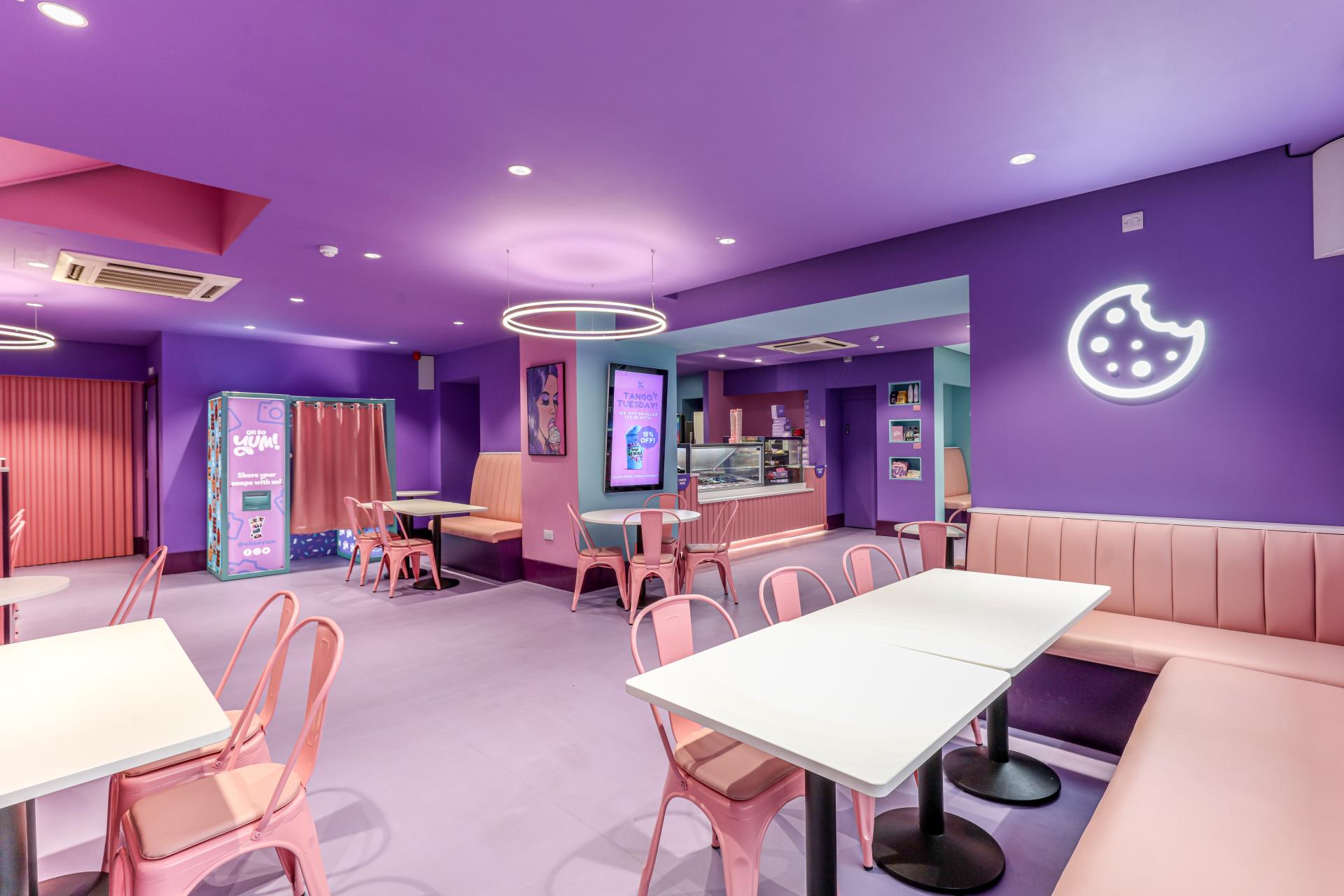 Brightly colored interior of Oh So Yum! in Bradford, featuring pink chairs, purple walls, and a cozy seating area.