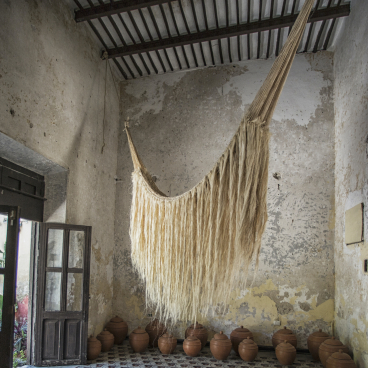 Handwoven Mexican hammock hangs in a rustic indoor space, surrounded by traditional clay pots, showcasing local craftsmanship.