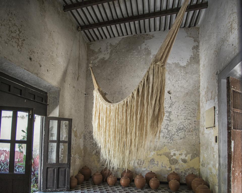 Handwoven Mexican hammock hangs in a rustic indoor space, surrounded by traditional clay pots, showcasing local craftsmanship.