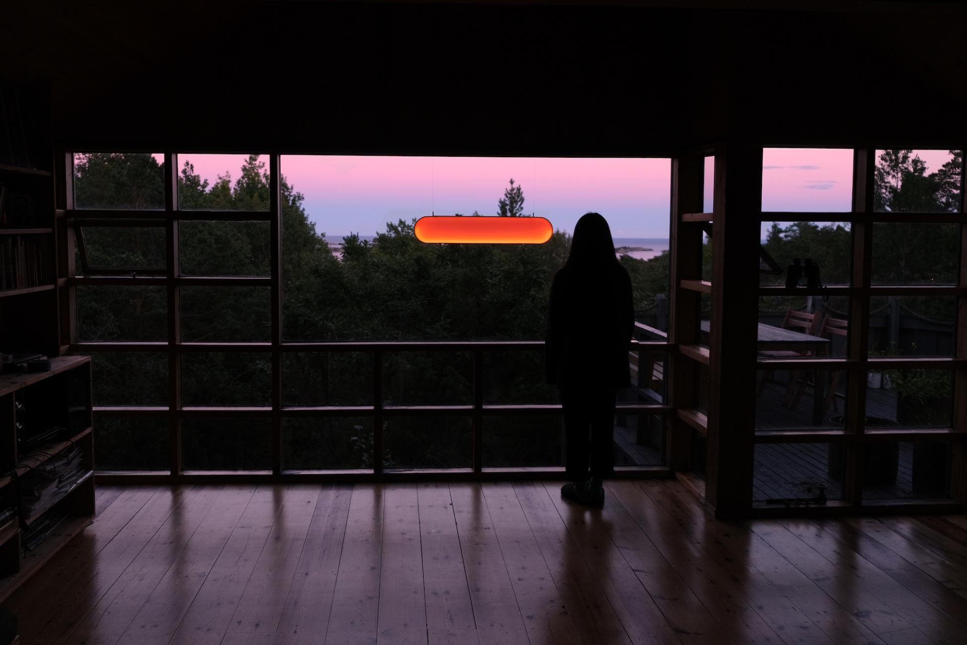 Silhouette of a person gazing at a scenic sunset through large windows, highlighting color contrasts in design.