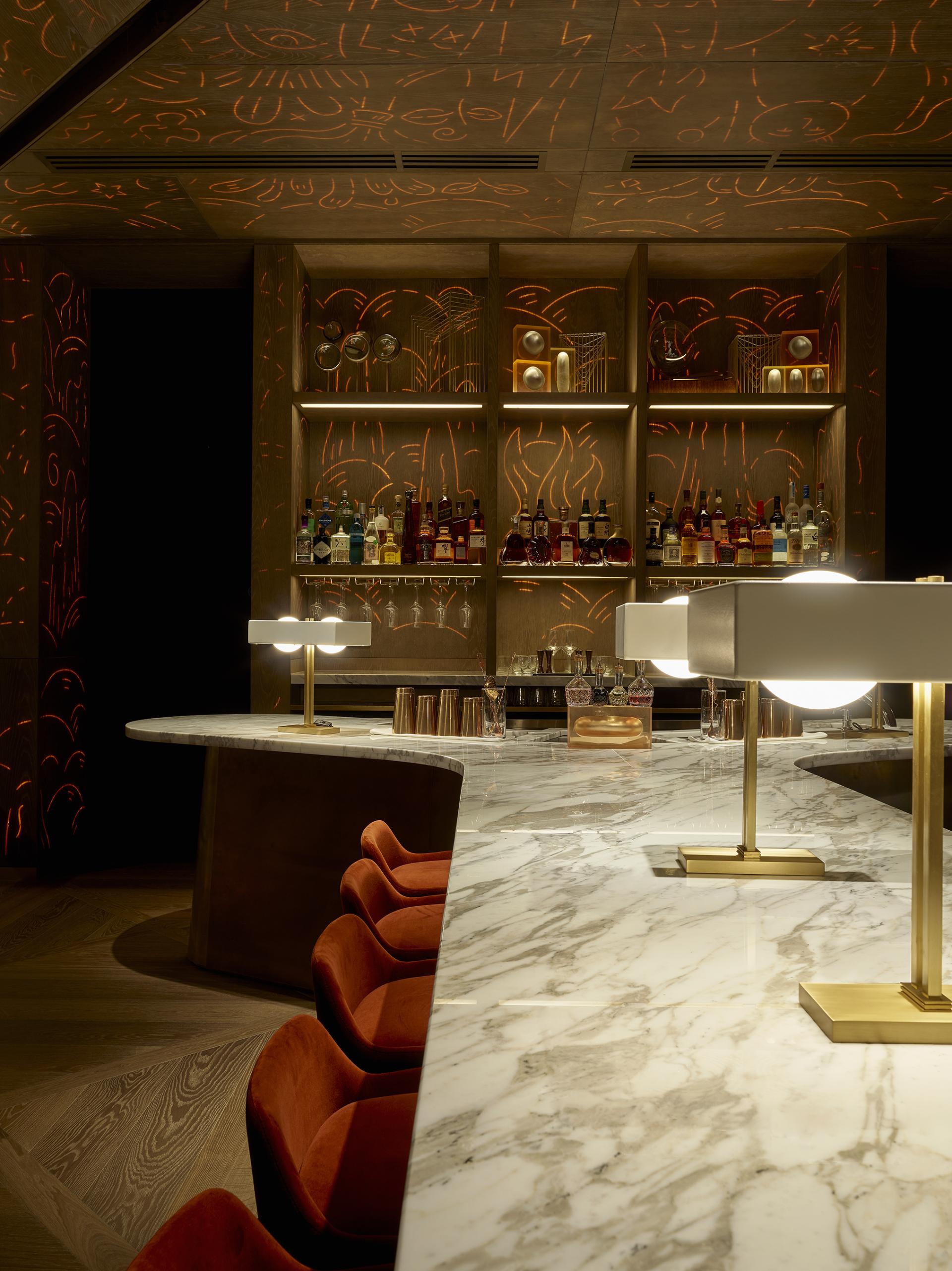 Elegant bar interior at Leicester Square hotel, featuring a marble countertop, stylish lighting, and creative wall designs.
